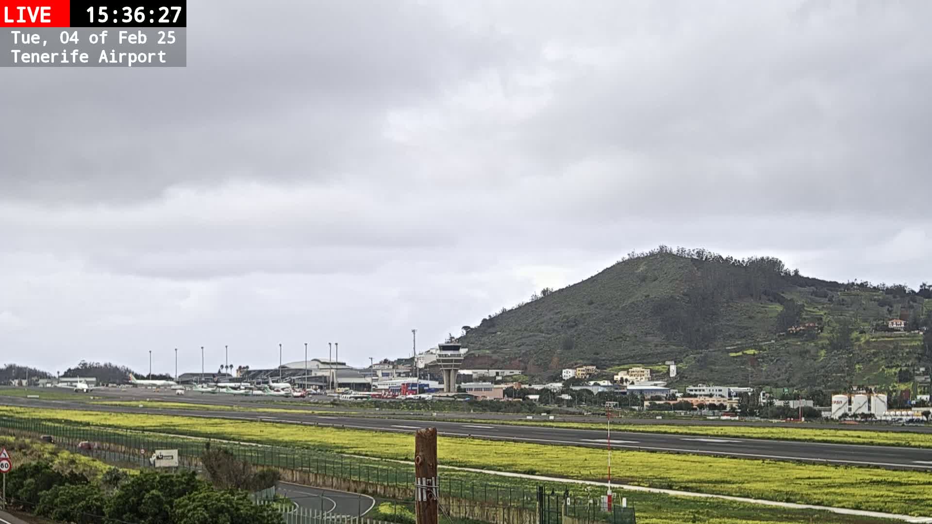 An airport runway with several airplanes is visible under an overcast sky, with a green hill in the background.
