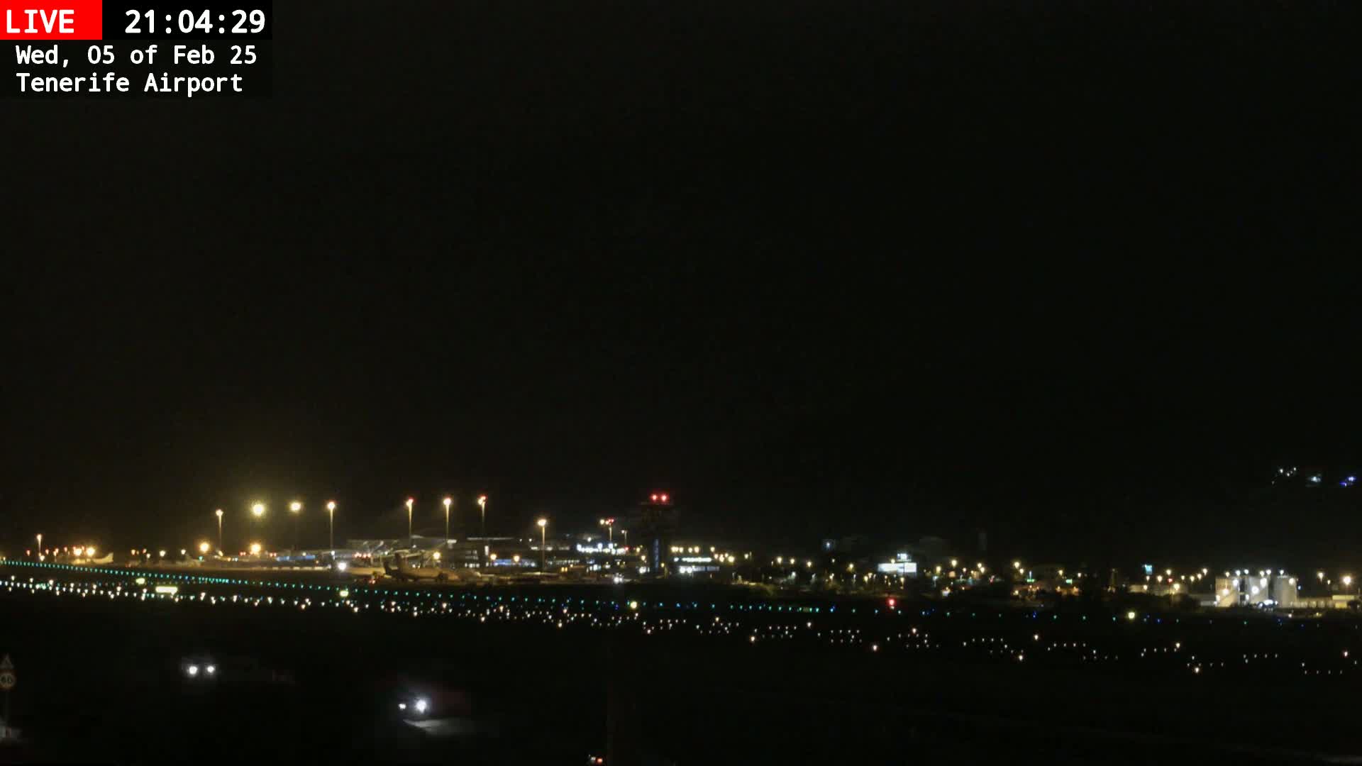 A nighttime long shot of an airport runway and terminal buildings illuminated under a dark, clear sky.