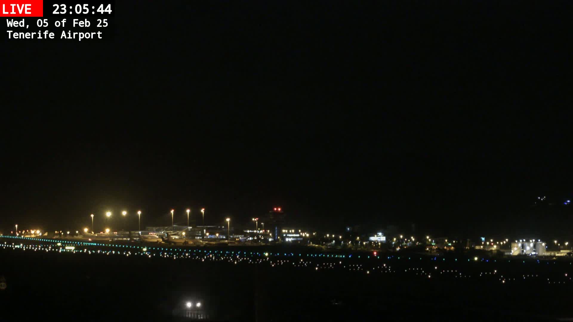 A nighttime long shot of an airport runway and terminal buildings illuminated under a clear, dark sky.
