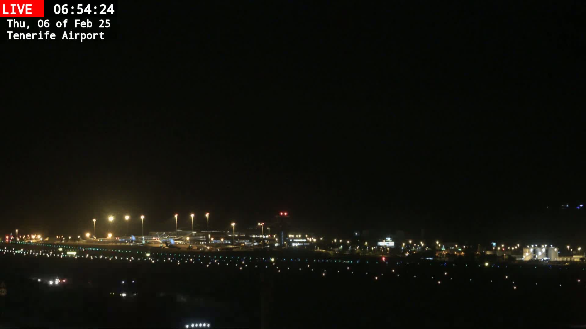 A nighttime long shot of an airport runway and terminal buildings illuminated by lights under a clear, dark sky.