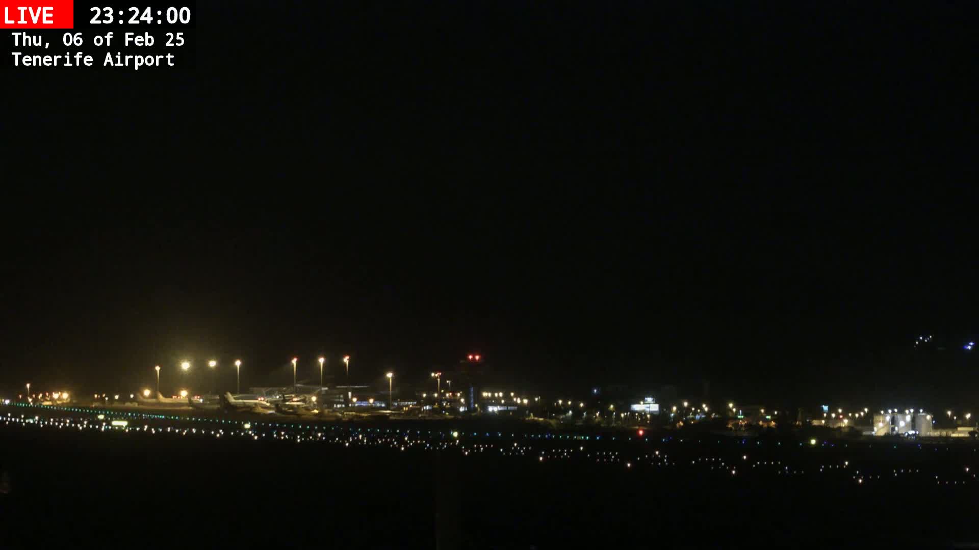 A nighttime view of an airport runway and terminal buildings illuminated by lights under a clear, dark sky.