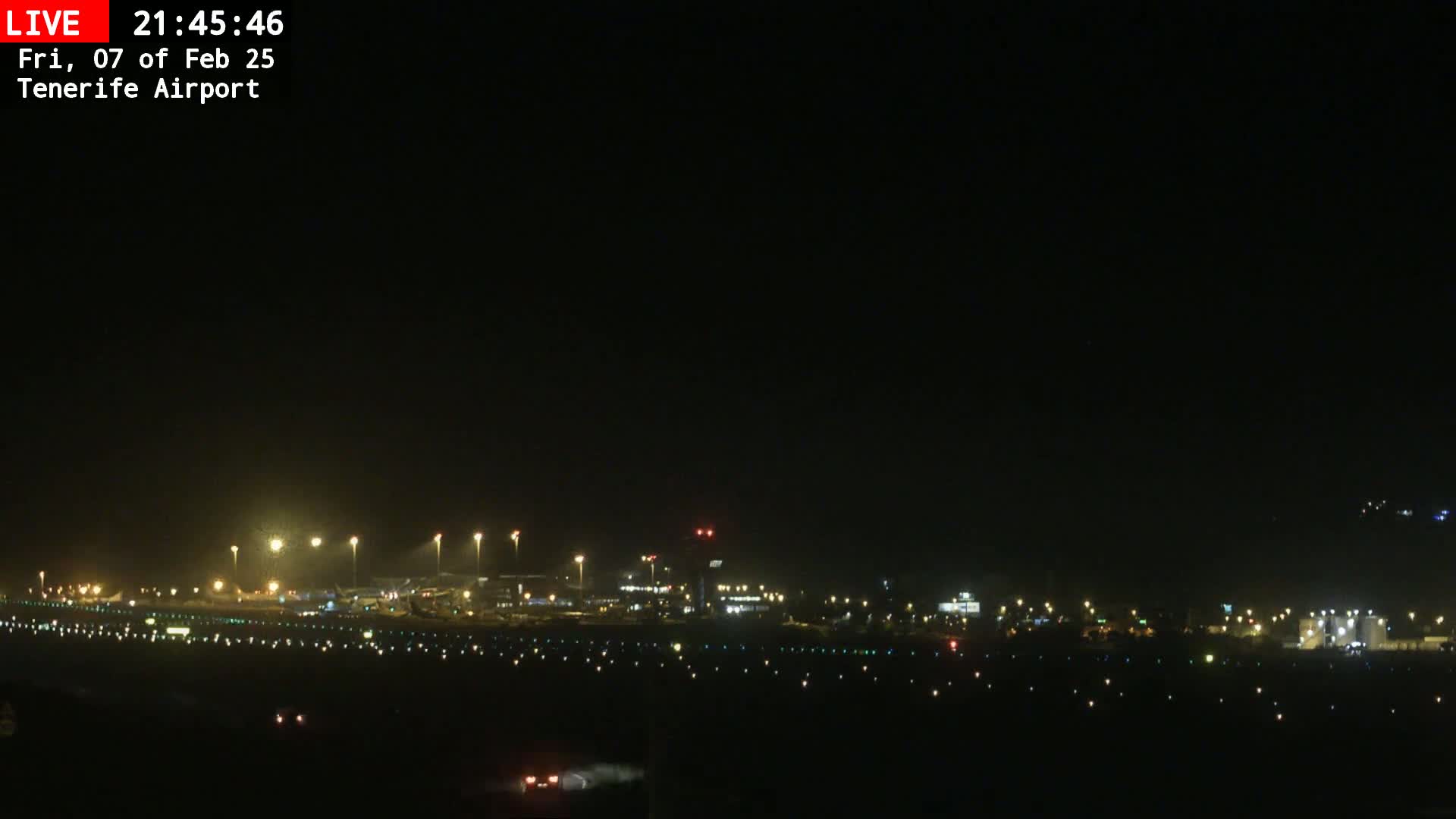 A nighttime, long shot of an airport runway and terminal buildings illuminated by lights under a clear, dark sky.