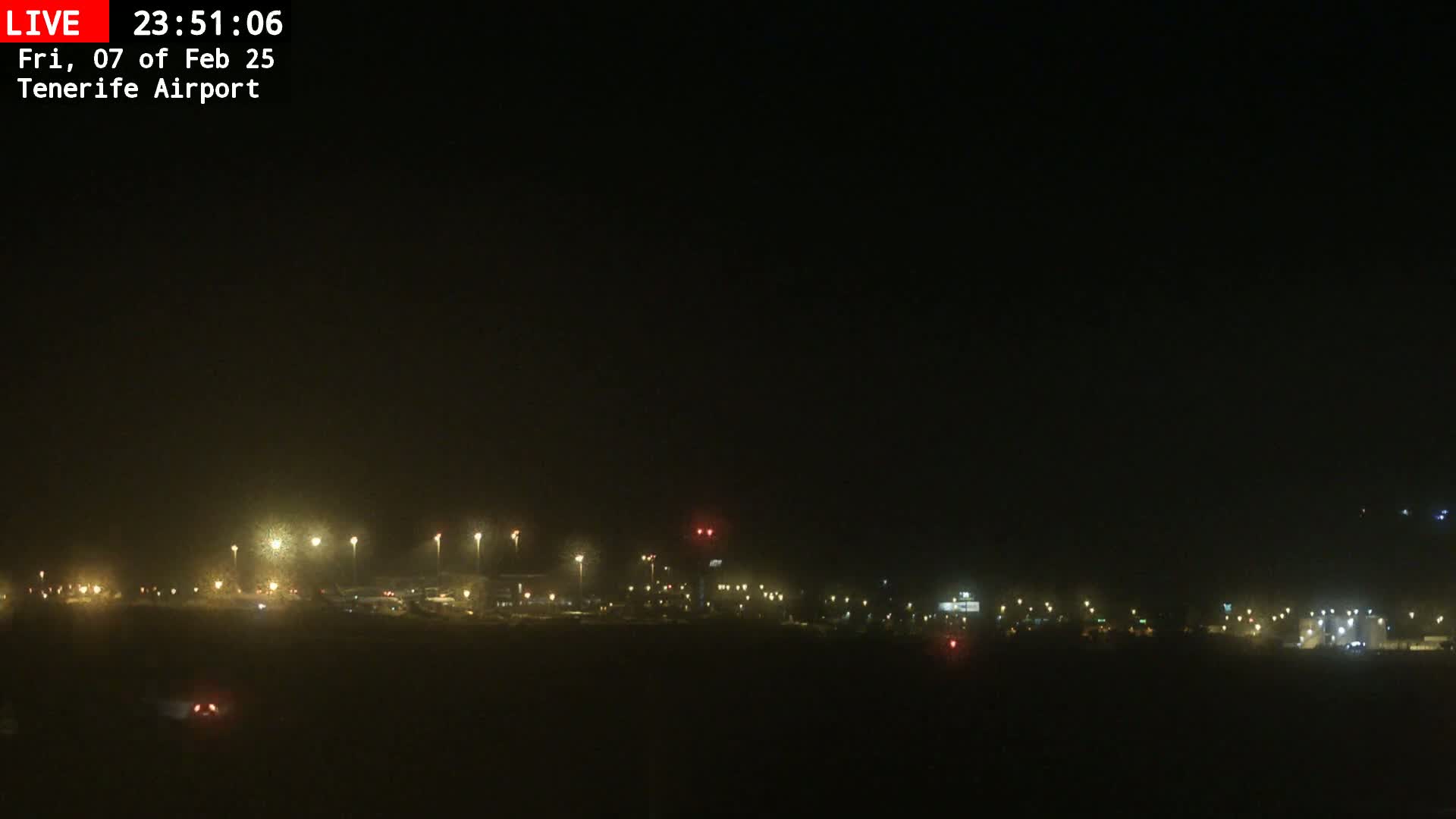 A nighttime view of an airport runway and surrounding buildings illuminated by many lights under a dark sky.