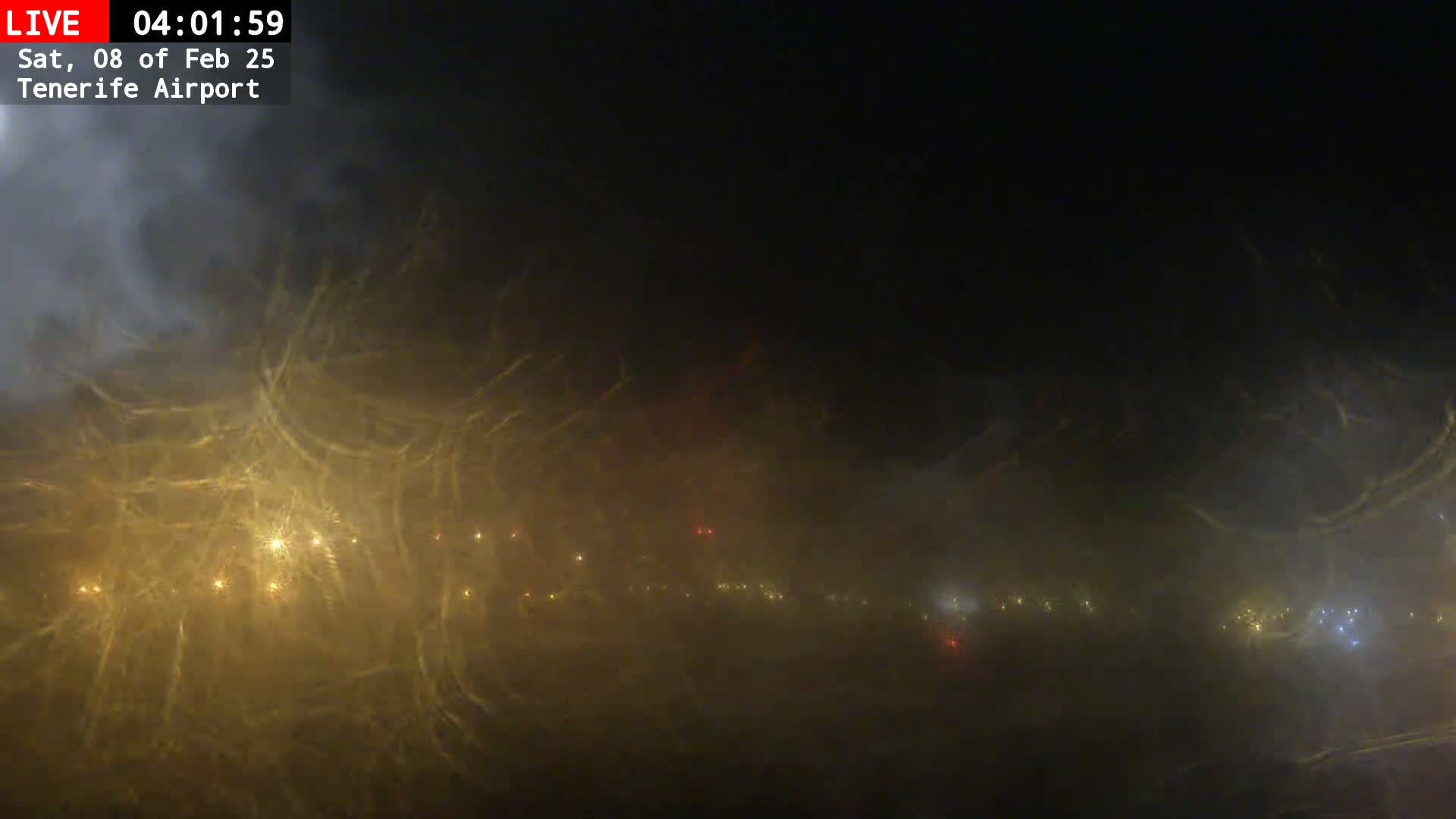 A nighttime view of a foggy airport runway with dim lights visible through the haze.