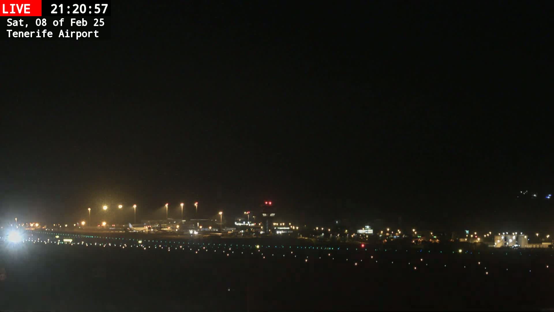 A nighttime view of an airport runway with several aircraft and terminal buildings illuminated under a clear, dark sky.
