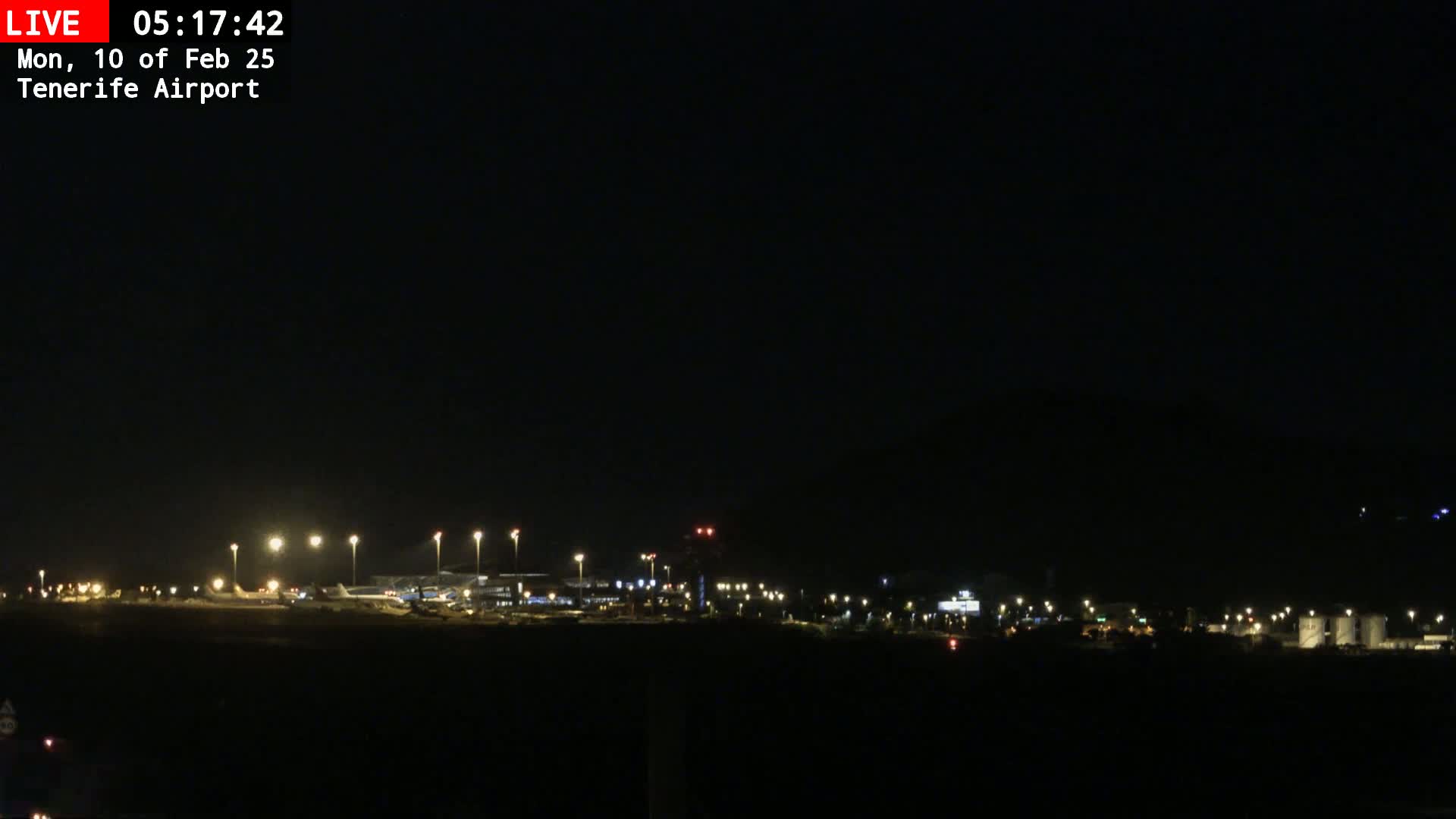 A nighttime view of an airport with dimly lit planes and buildings under a clear, dark sky.