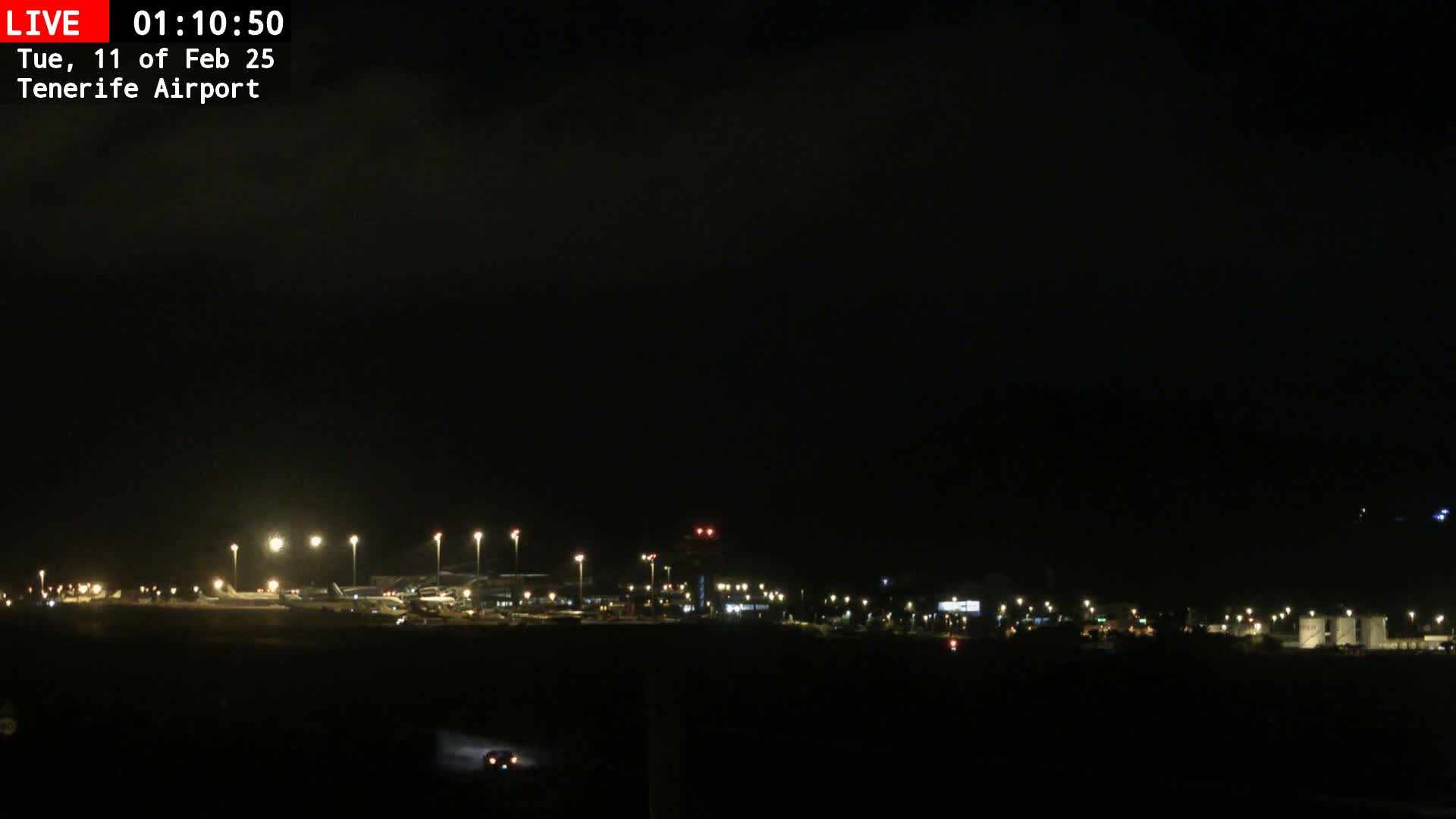 A nighttime long shot of a dimly lit airport under a dark, cloudy sky.