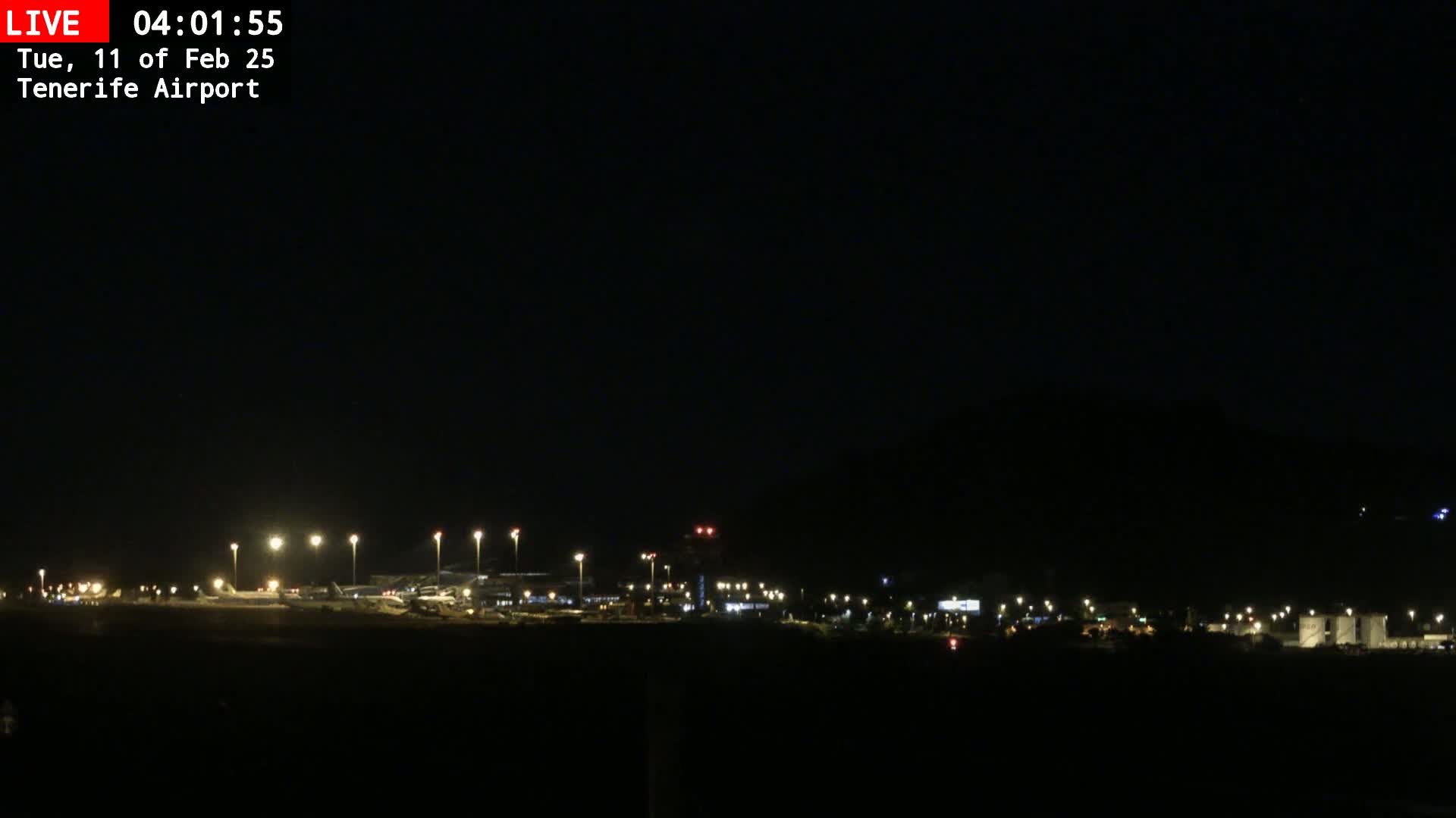 A nighttime long shot of an airport runway and terminal buildings illuminated under a clear, dark sky.