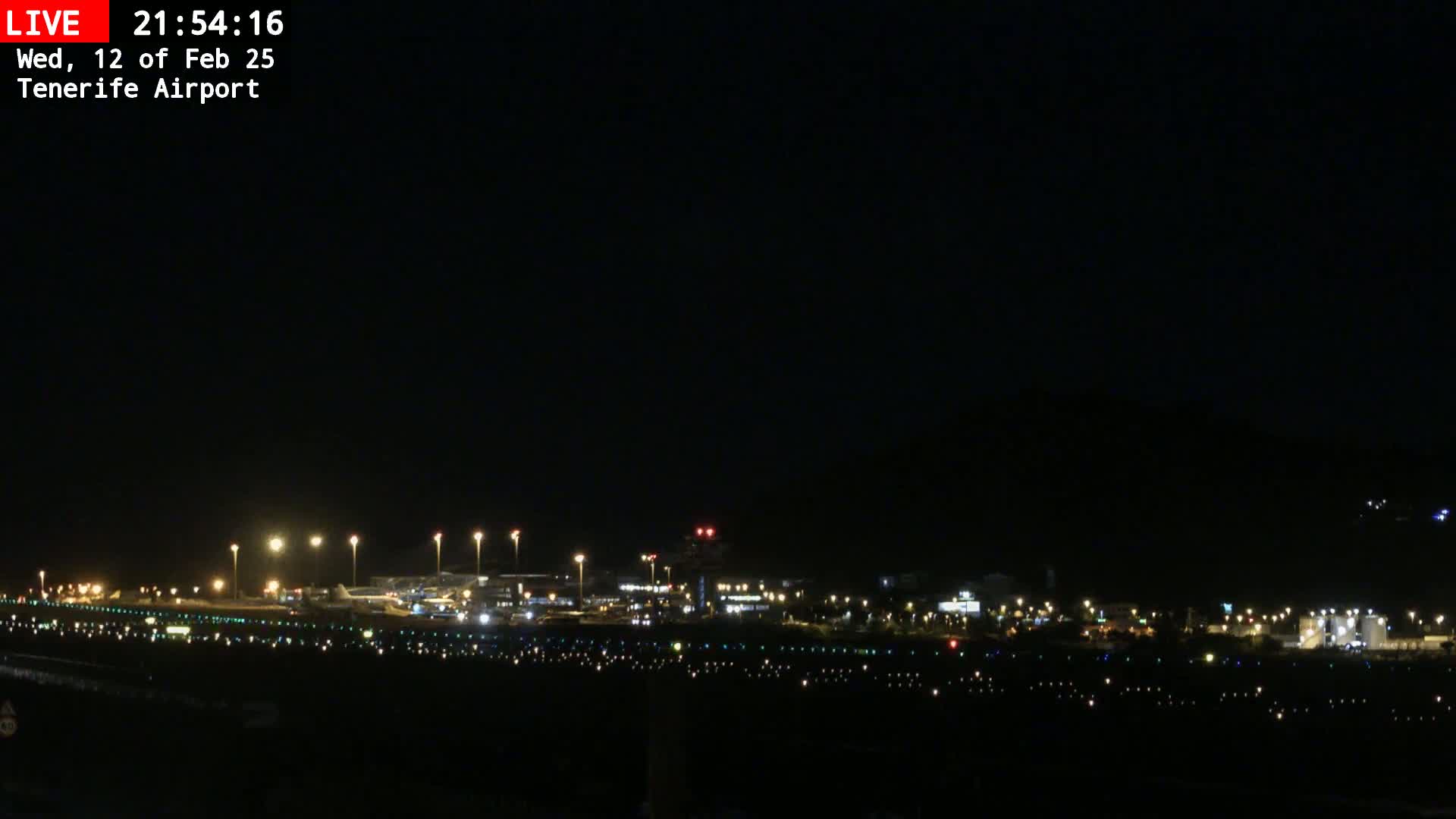 A nighttime view of an airport runway and terminal buildings illuminated by numerous lights against a dark, clear sky.