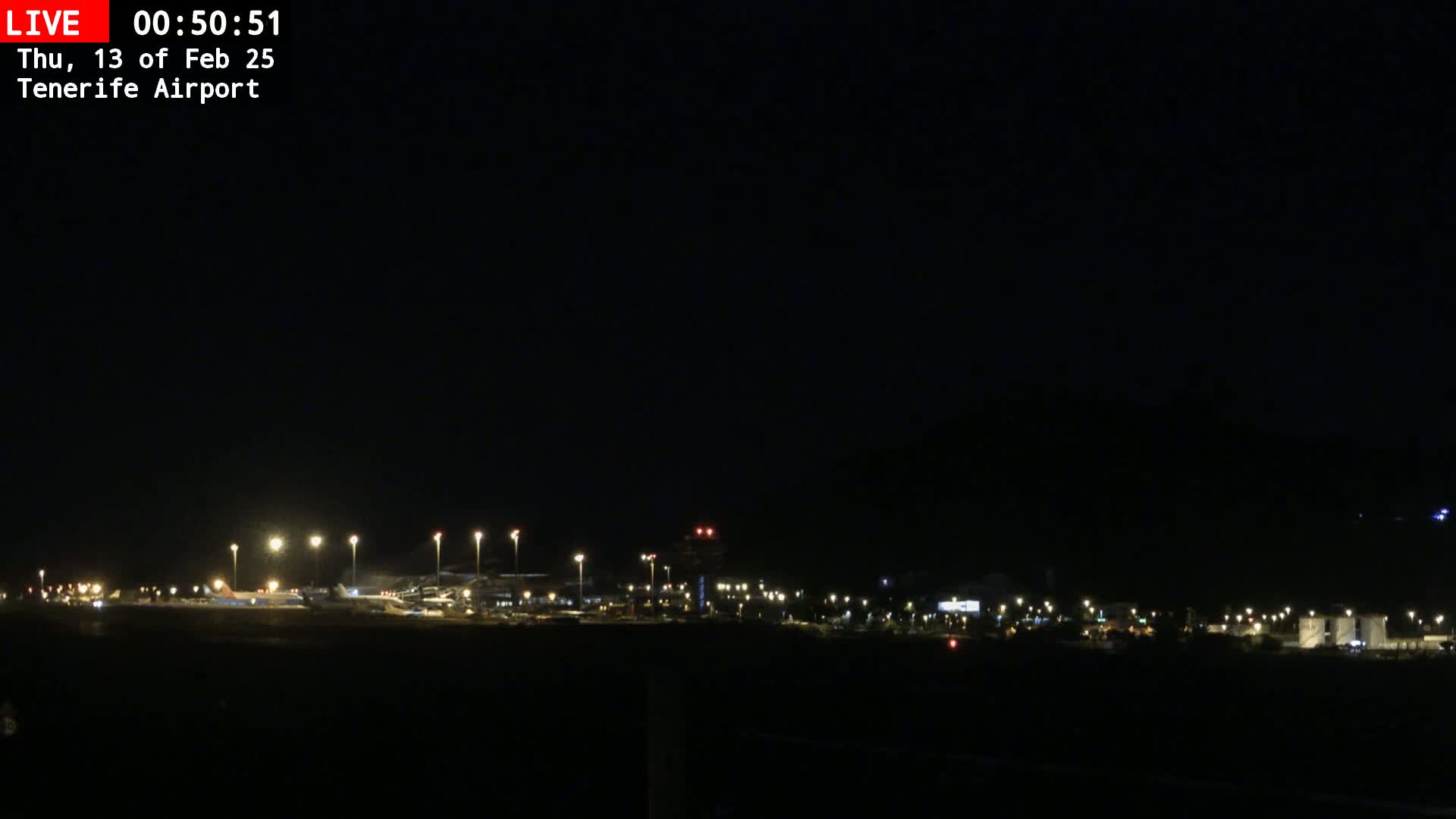 A nighttime view of an airport runway and terminal buildings illuminated by numerous lights under a clear, dark sky.