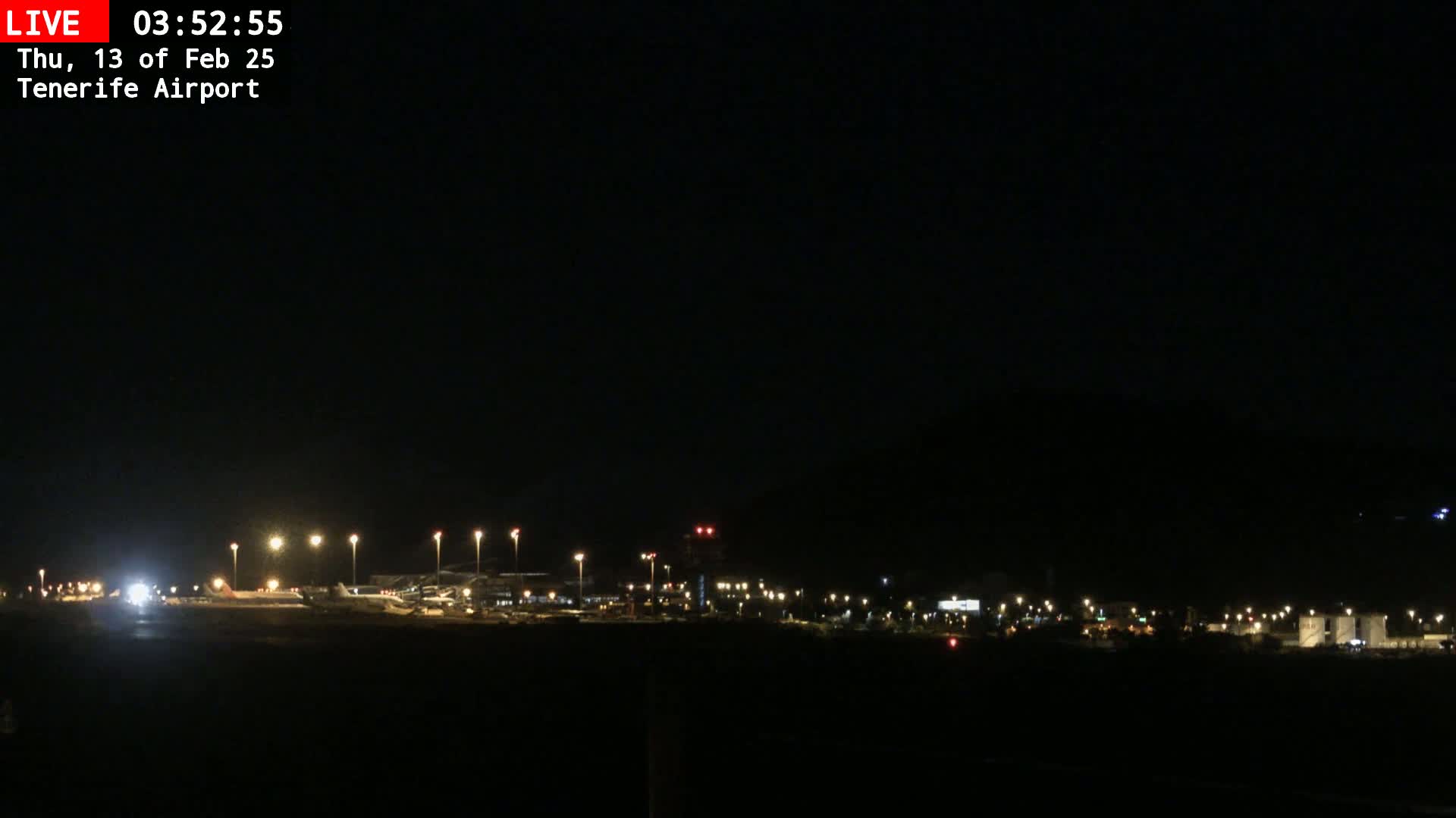 A nighttime view of an airport tarmac, illuminated by runway lights, with a dark sky above.