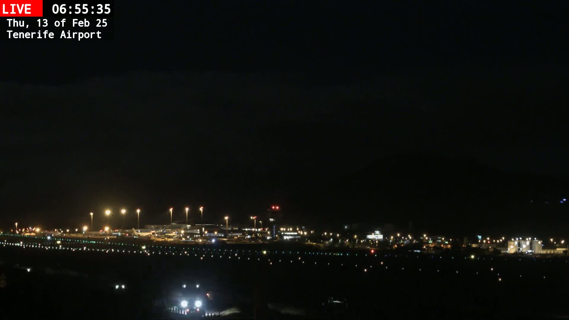 A nighttime long shot of an airport runway and terminal buildings illuminated under a dark, clear sky.