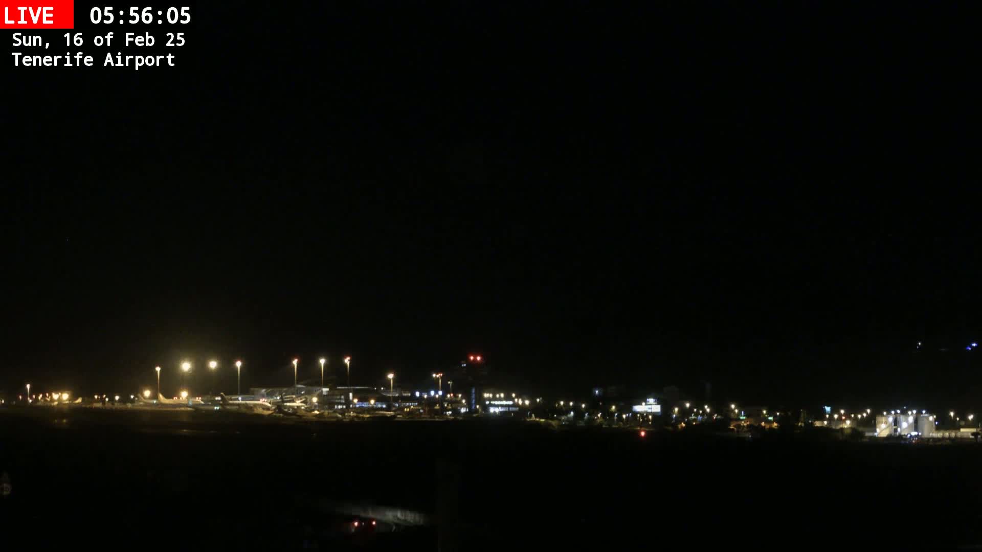 A nighttime view of an airport with lights illuminating the tarmac and buildings under a clear, dark sky.