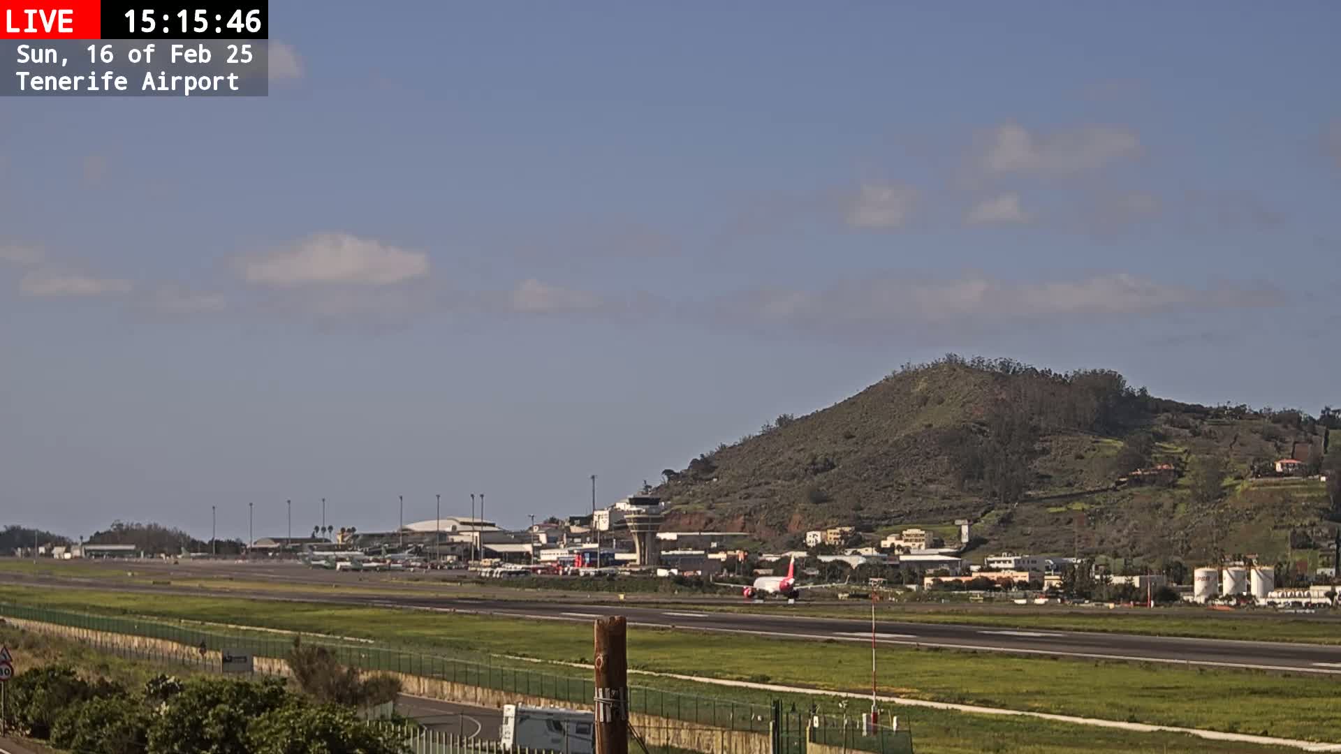 A passenger plane taxis on a runway at an airport near a hill under a partly cloudy sky.