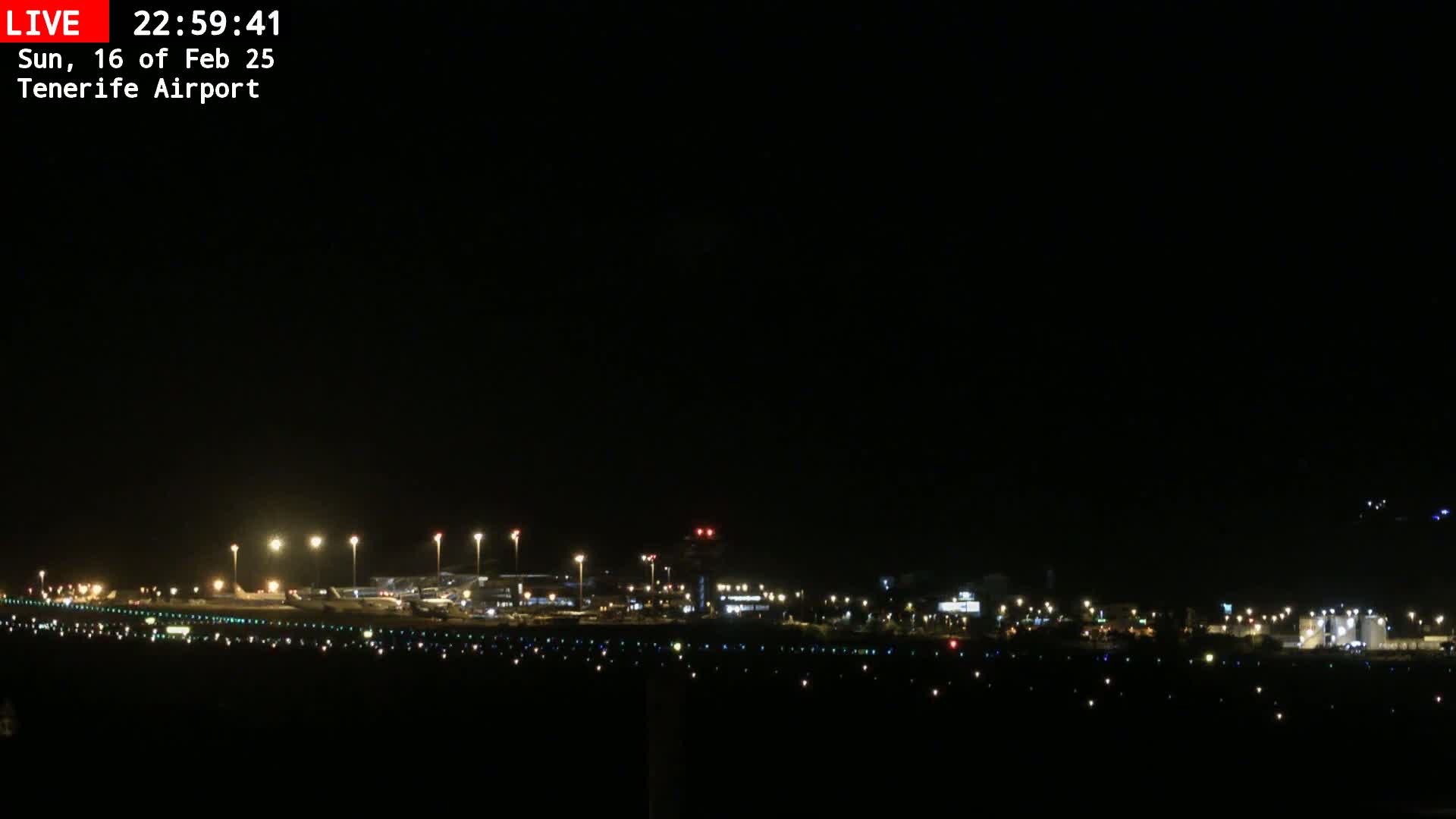 A nighttime view of an airport runway and terminal buildings illuminated by lights under a clear, dark sky.