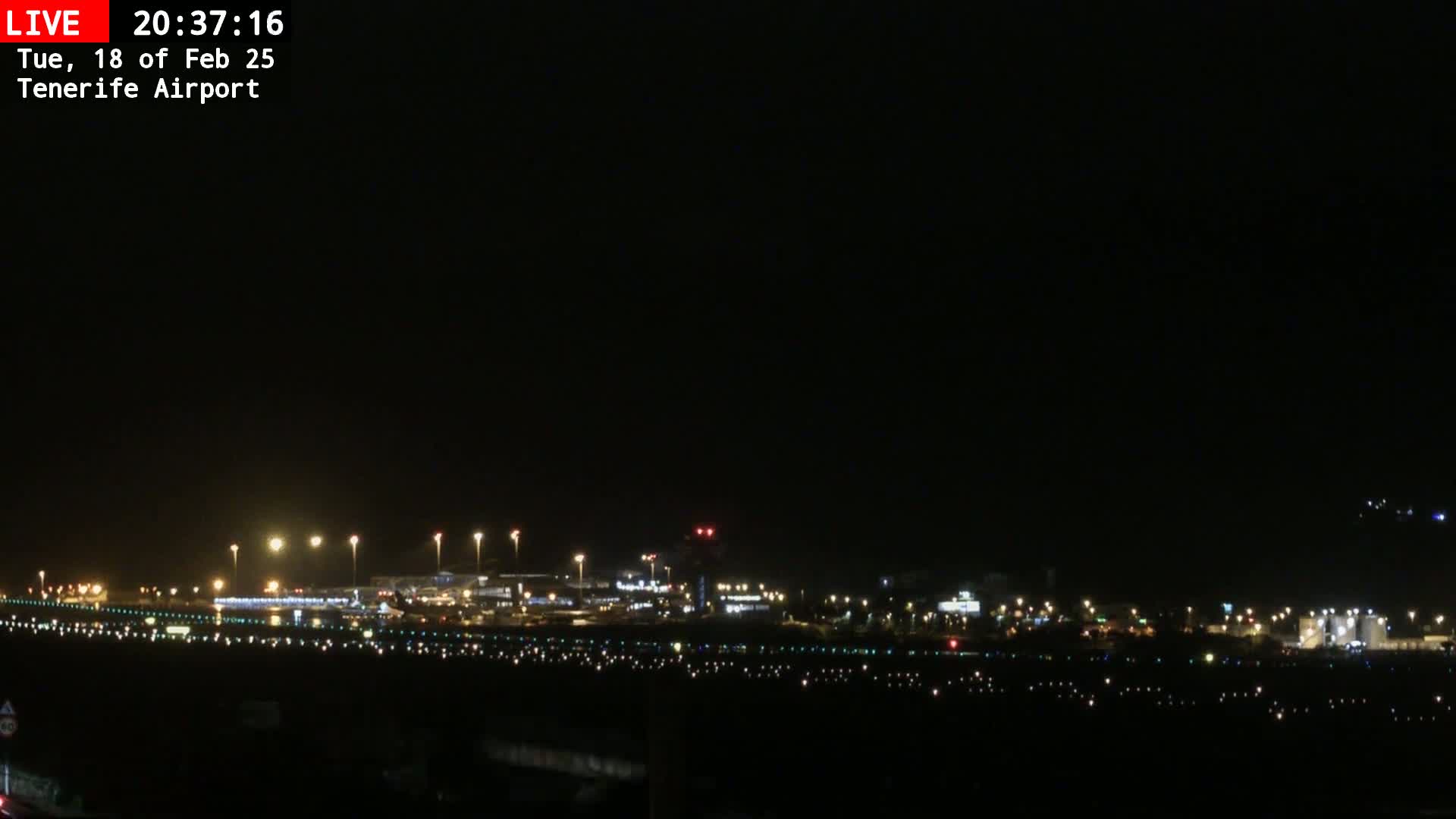 A nighttime long shot of an airport runway and terminal buildings illuminated by lights under a dark sky.
