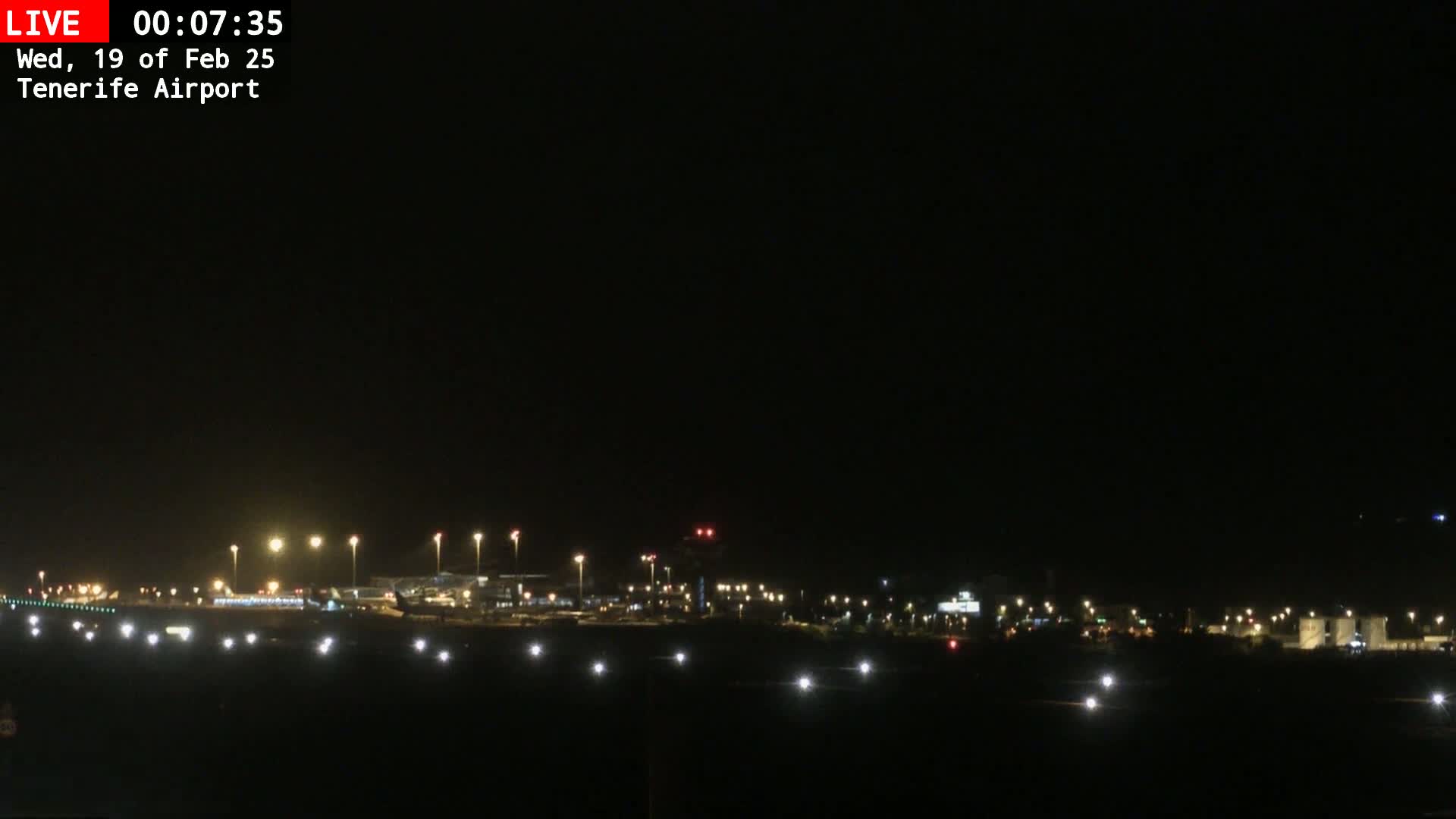 A nighttime view of an airport runway and terminal buildings illuminated by numerous lights under a clear, dark sky.