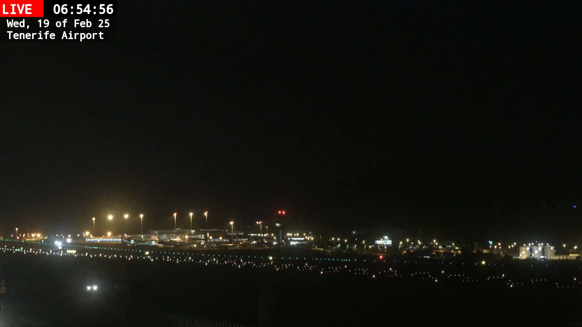 A nighttime long shot of an airport runway and terminal buildings illuminated under a dark, clear sky.