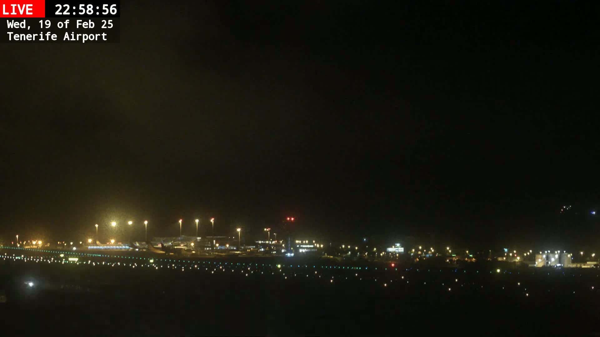 A nighttime, dimly lit view of an airport runway and terminal buildings under a dark sky.