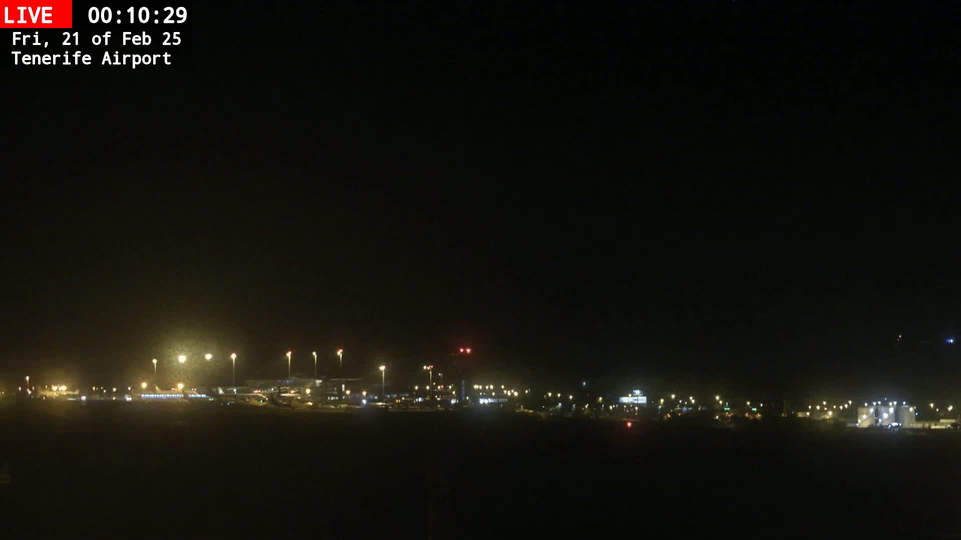 A nighttime view of an airport runway and terminal buildings illuminated by numerous lights under a clear, dark sky.
