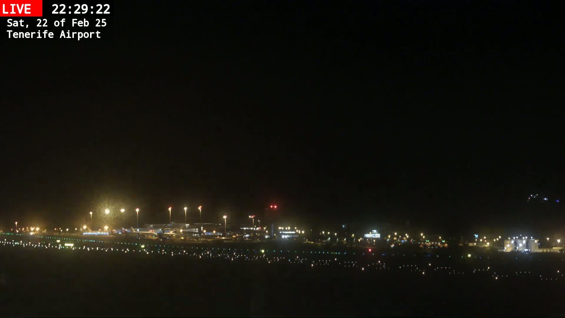 A nighttime view of an airport runway and terminal buildings illuminated by lights under a dark sky.