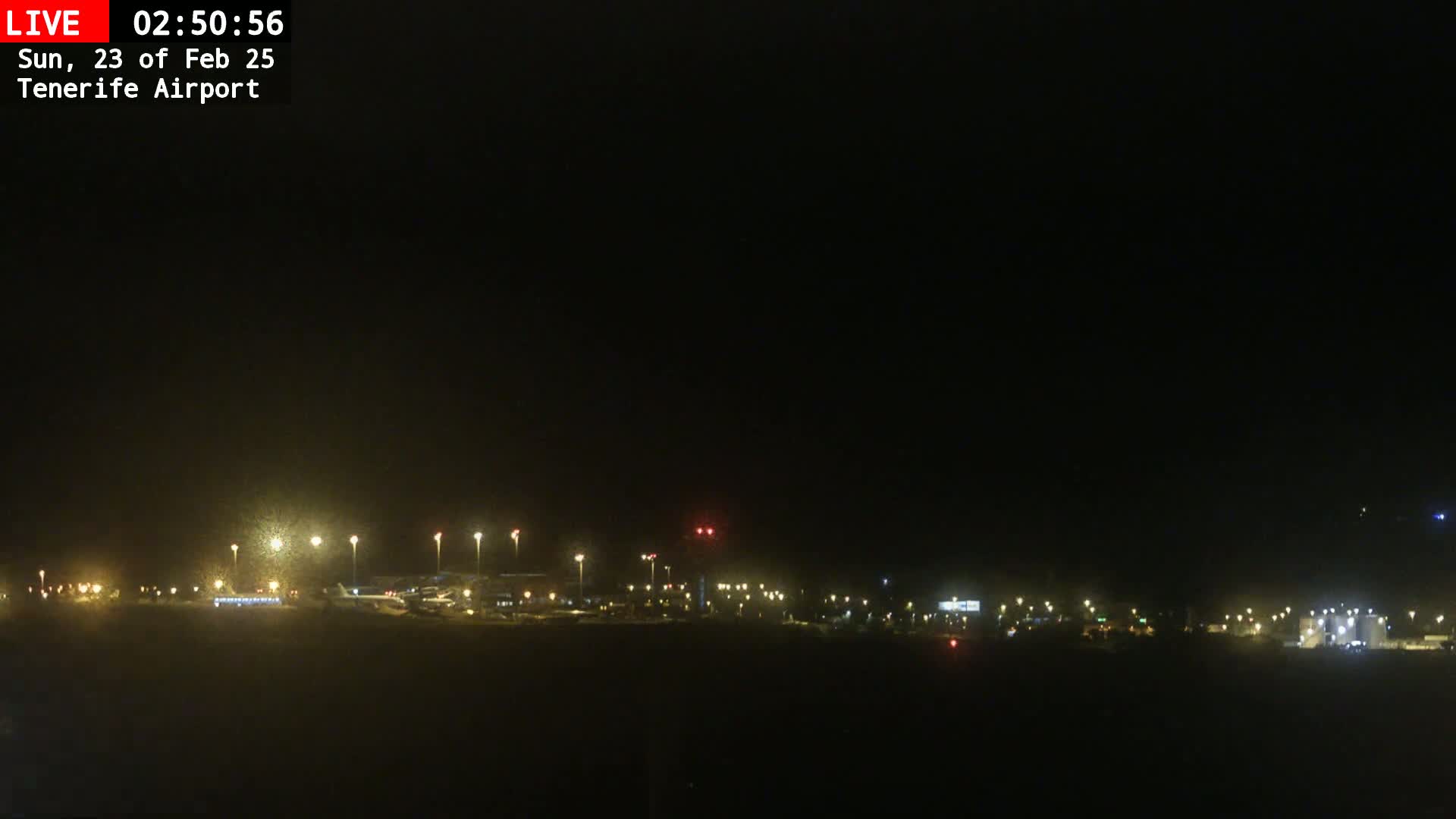 A nighttime view of an airport tarmac with dimly lit planes and buildings under a dark sky.