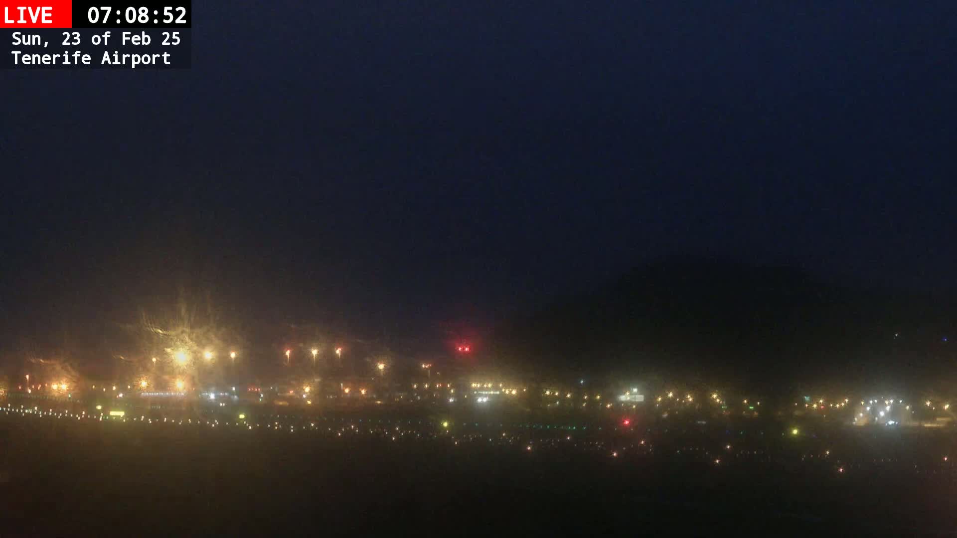A nighttime view of an airport runway and surrounding area, obscured by a hazy atmosphere.