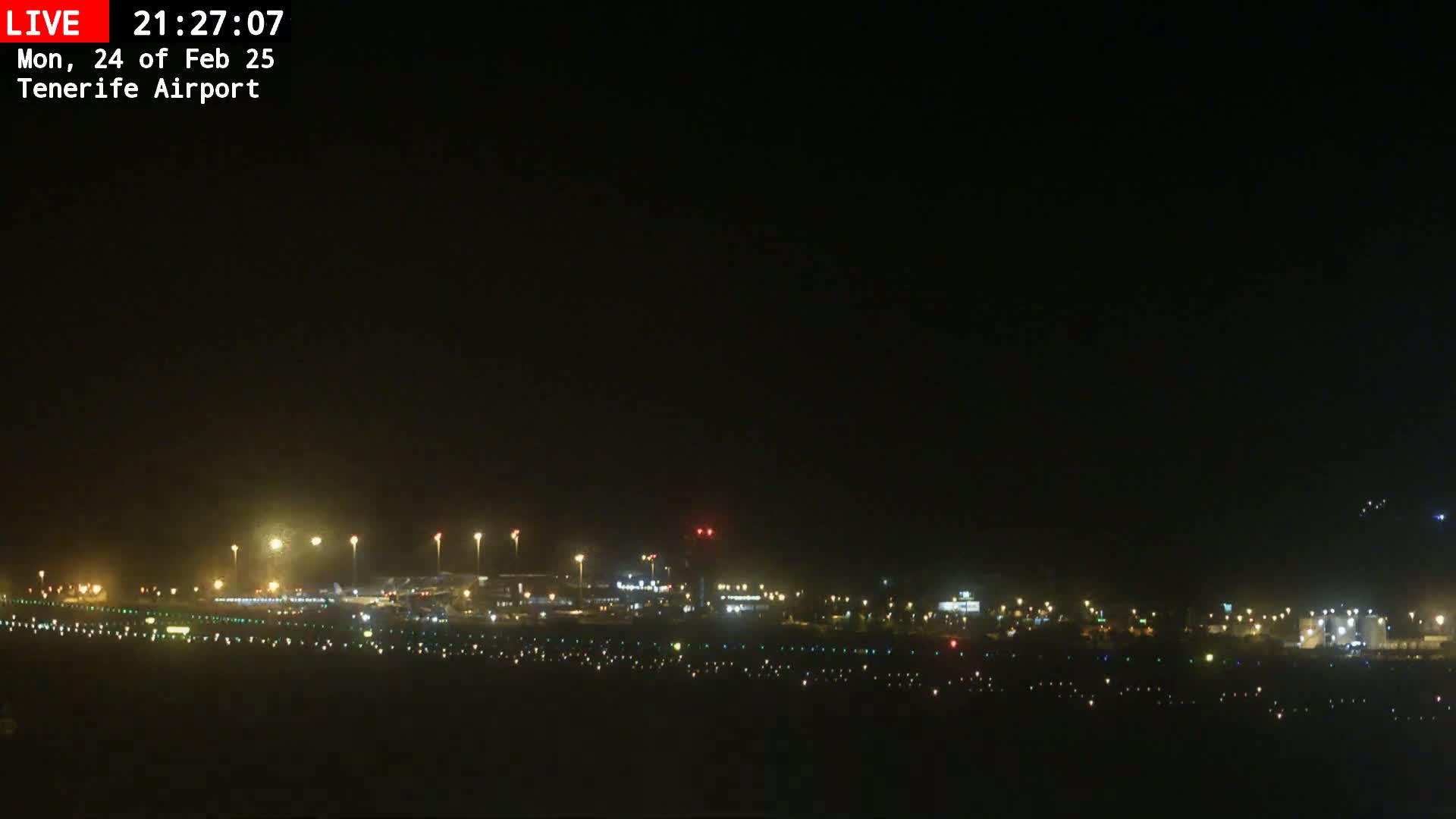 A nighttime long shot of an airport runway and terminal buildings illuminated by many lights under a clear, dark sky.