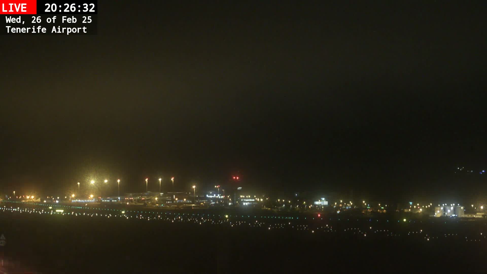 A nighttime view of a dimly lit airport runway and terminal buildings under hazy or foggy conditions.