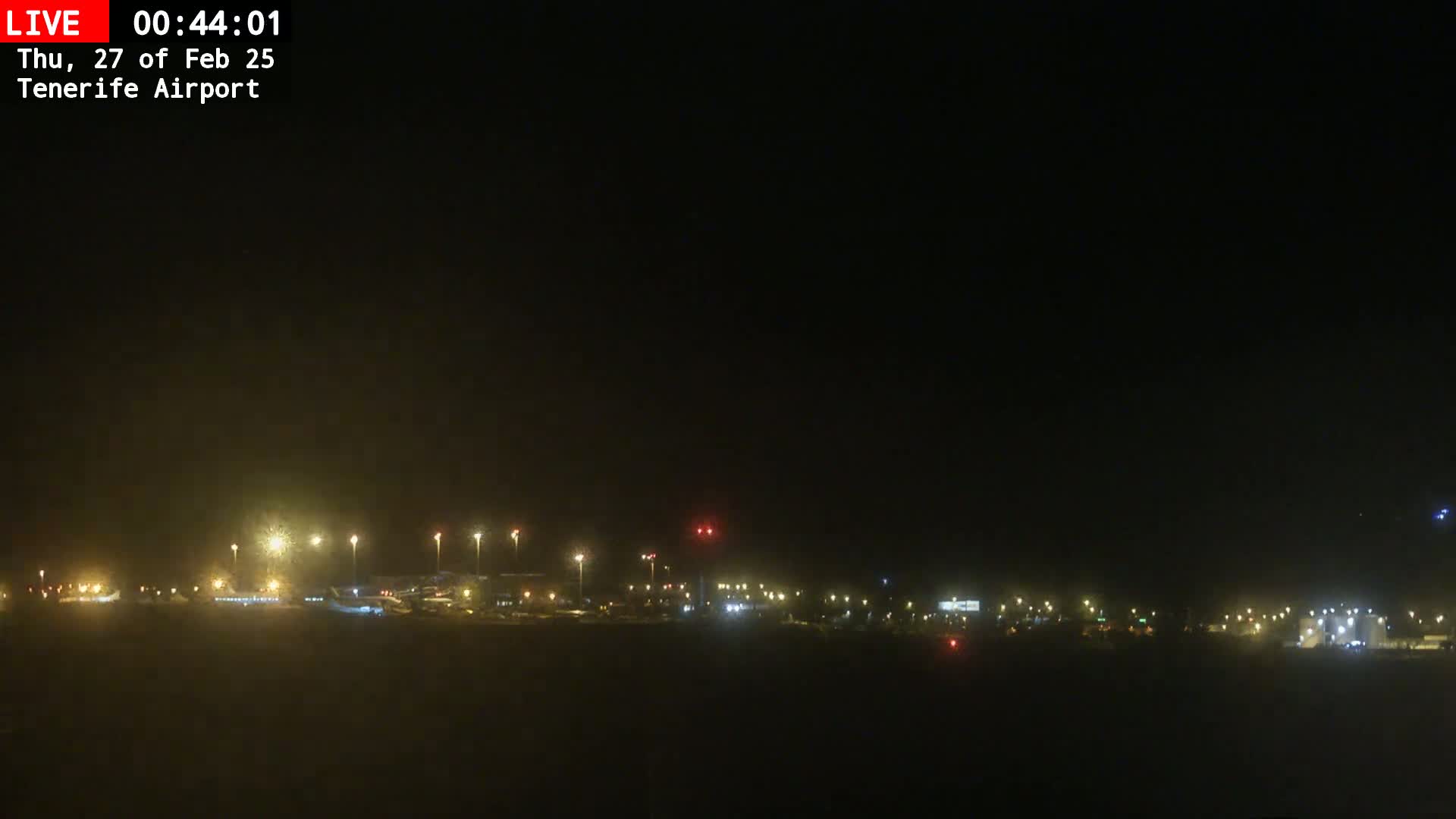 A nighttime view of an airport tarmac with several planes visible, under hazy or foggy conditions.