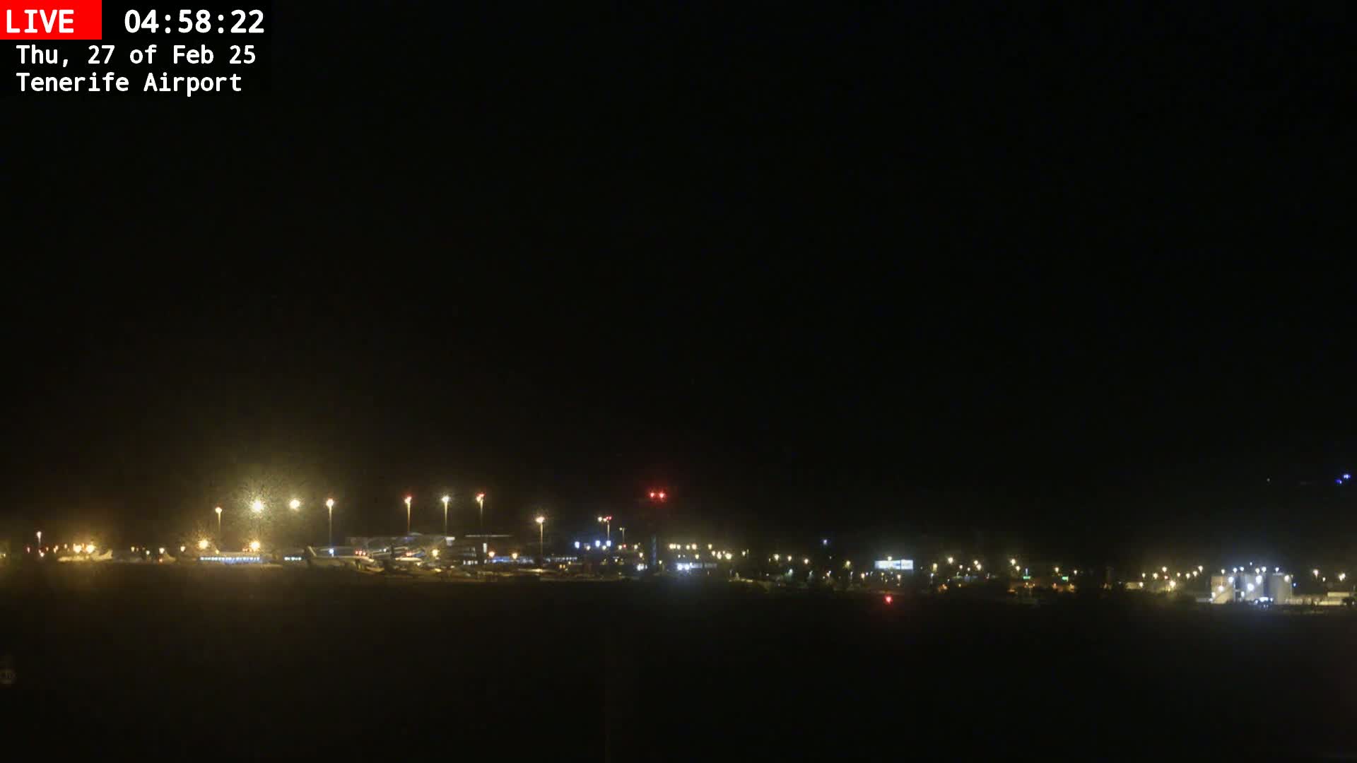 A nighttime long shot of an airport runway and terminal buildings dimly lit under a clear, dark sky.