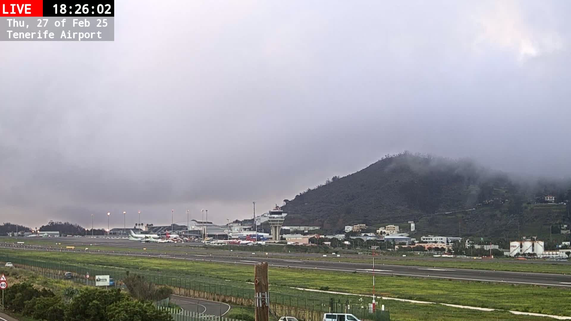 A foggy view of an airport runway, terminal buildings, and a hill shrouded in mist.