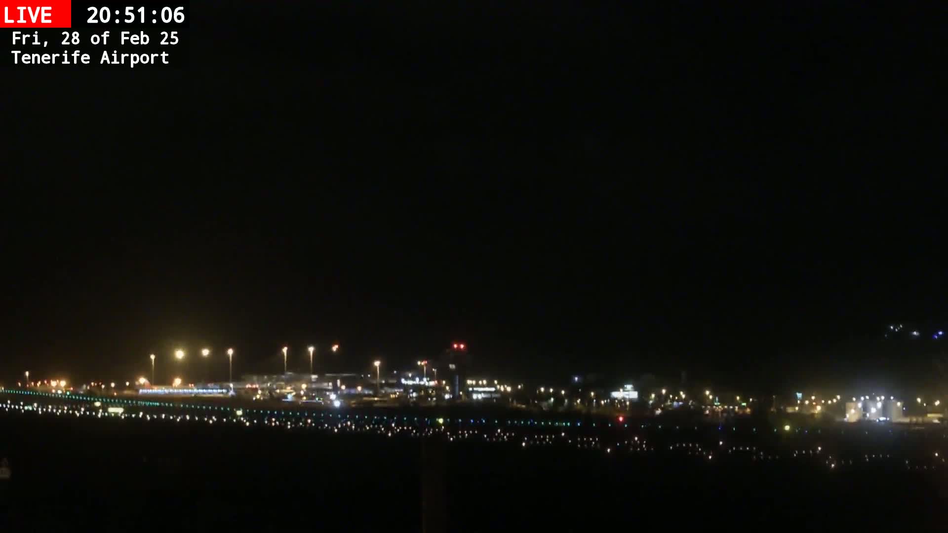 A nighttime view of an airport runway and terminal buildings illuminated by lights under a clear, dark sky.