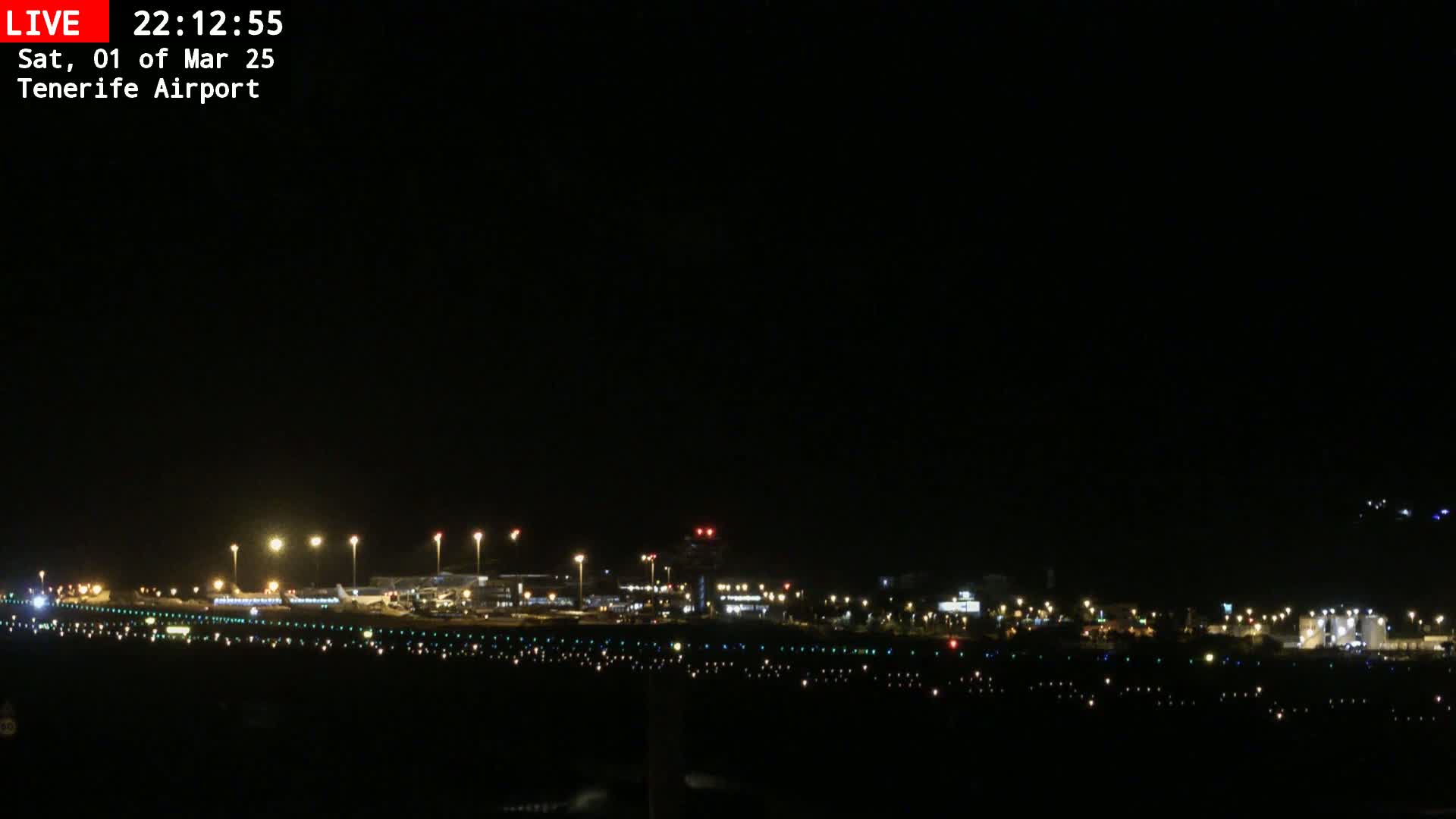 A nighttime view of an airport runway and terminal buildings illuminated by lights under a clear, dark sky.