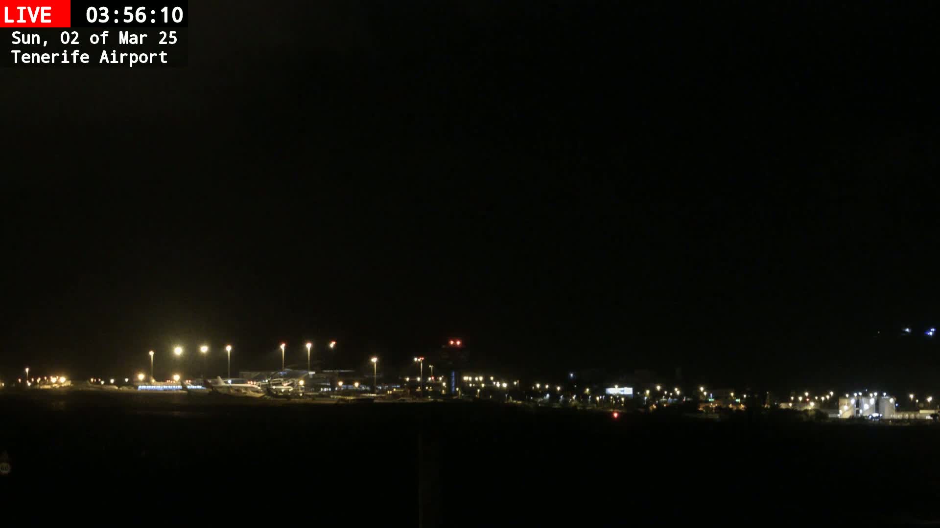 A nighttime view of an airport runway and terminal buildings illuminated by numerous lights under a dark, clear sky.