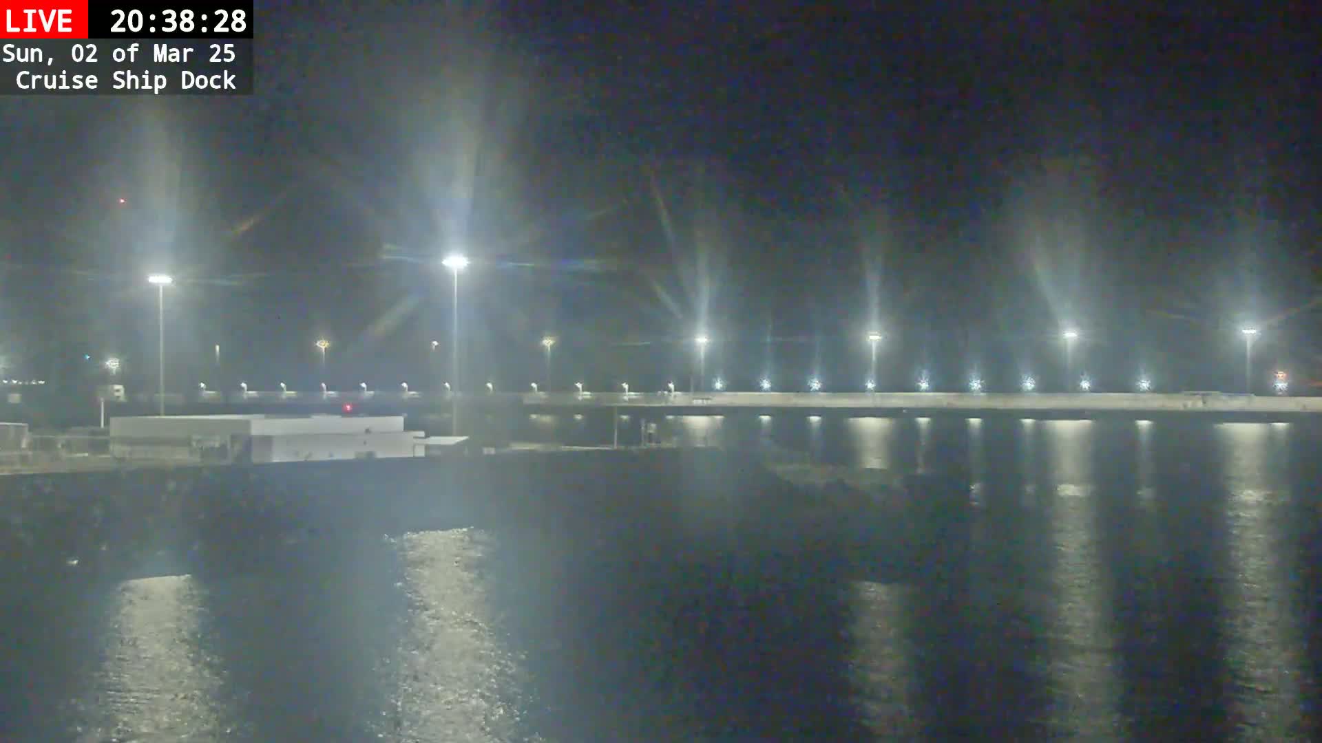 A nighttime view of a brightly lit cruise ship dock reflecting in calm water.