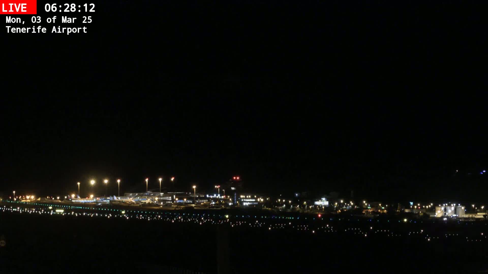 A nighttime view of an airport runway and terminal buildings illuminated by lights under a clear, dark sky.