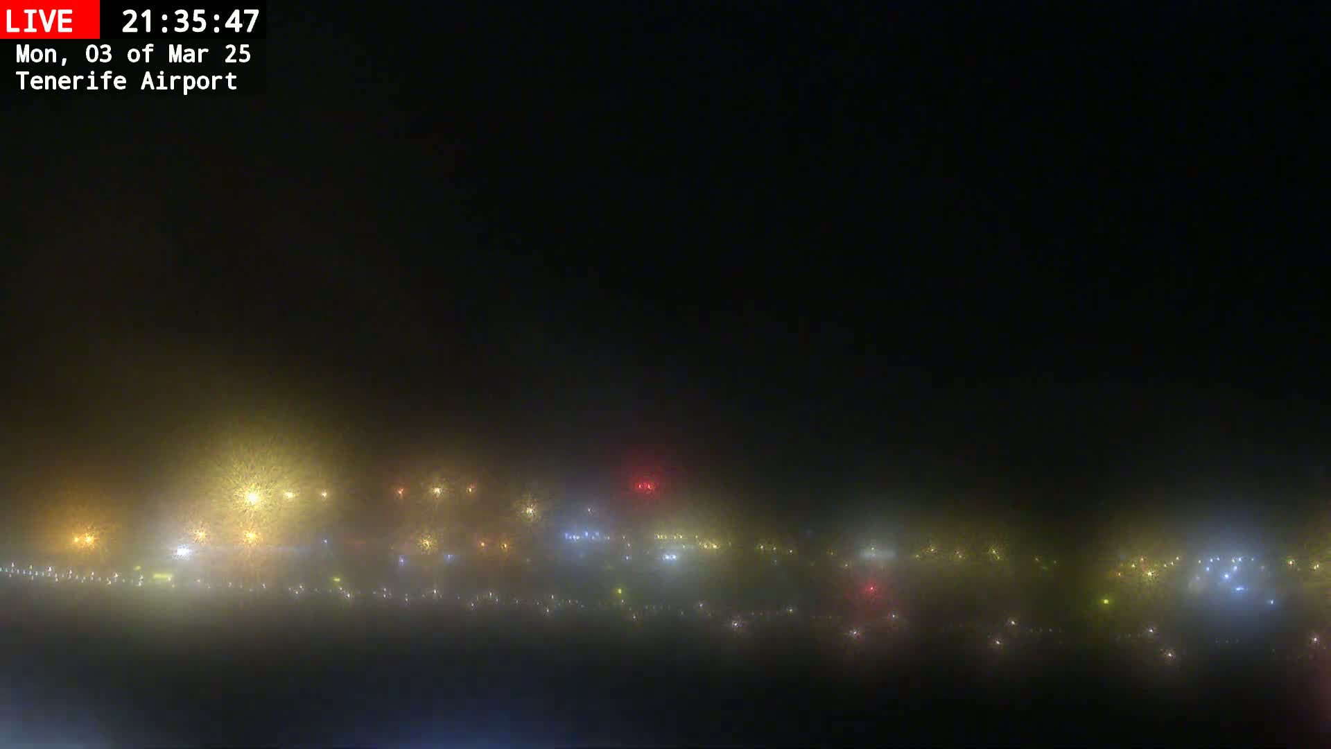 A foggy night scene shows numerous lights in the distance, appearing hazy and obscured by the fog.