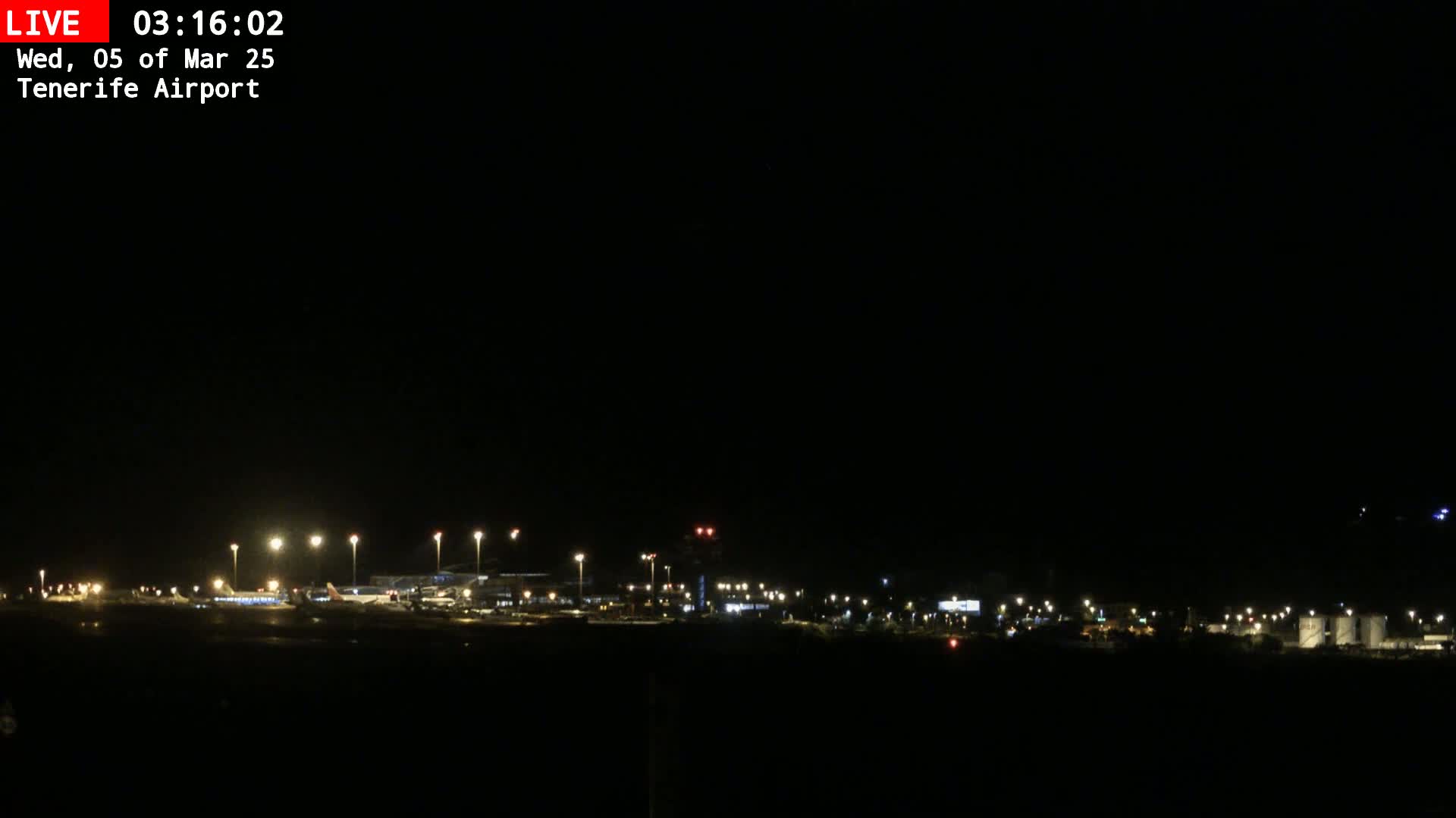 A nighttime long shot of an airport runway and terminal buildings illuminated by lights under a clear, dark sky.
