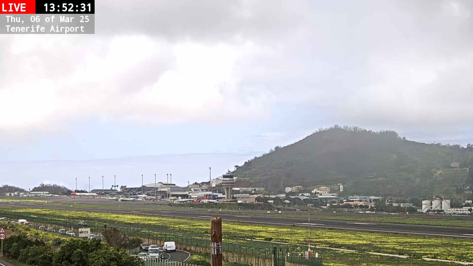 A hazy view of an airport runway, terminal buildings, and a hill in the background under an overcast sky.