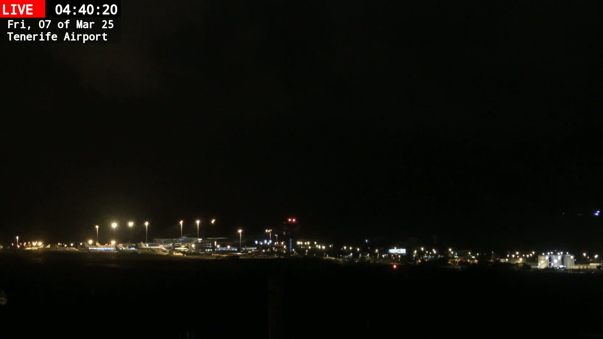 A nighttime view of an airport tarmac with several airplanes and illuminated buildings under a dark sky.