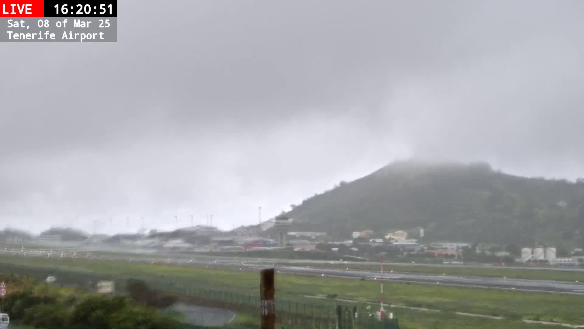 A rainy, overcast day at an airport with a hill visible in the background.