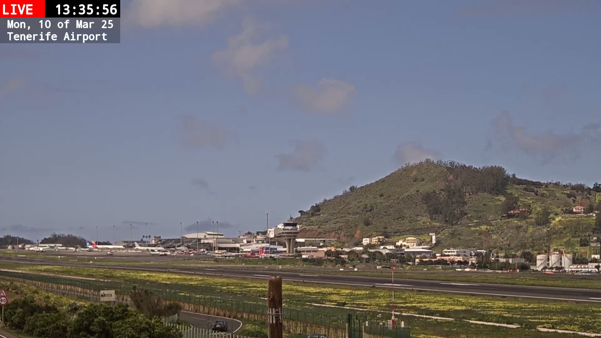 A mostly clear sky over an airport with several airplanes on the tarmac,  adjacent to a low, green hill.