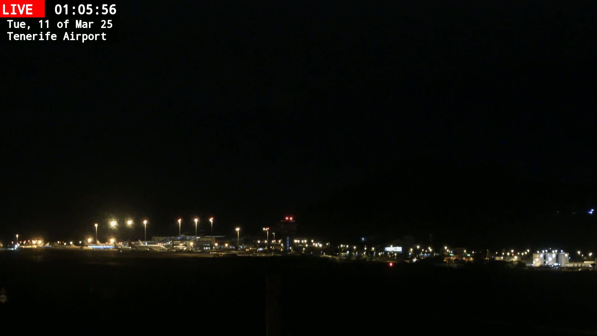 A nighttime long shot of an airport runway and terminal buildings illuminated by artificial lights under a clear, dark sky.