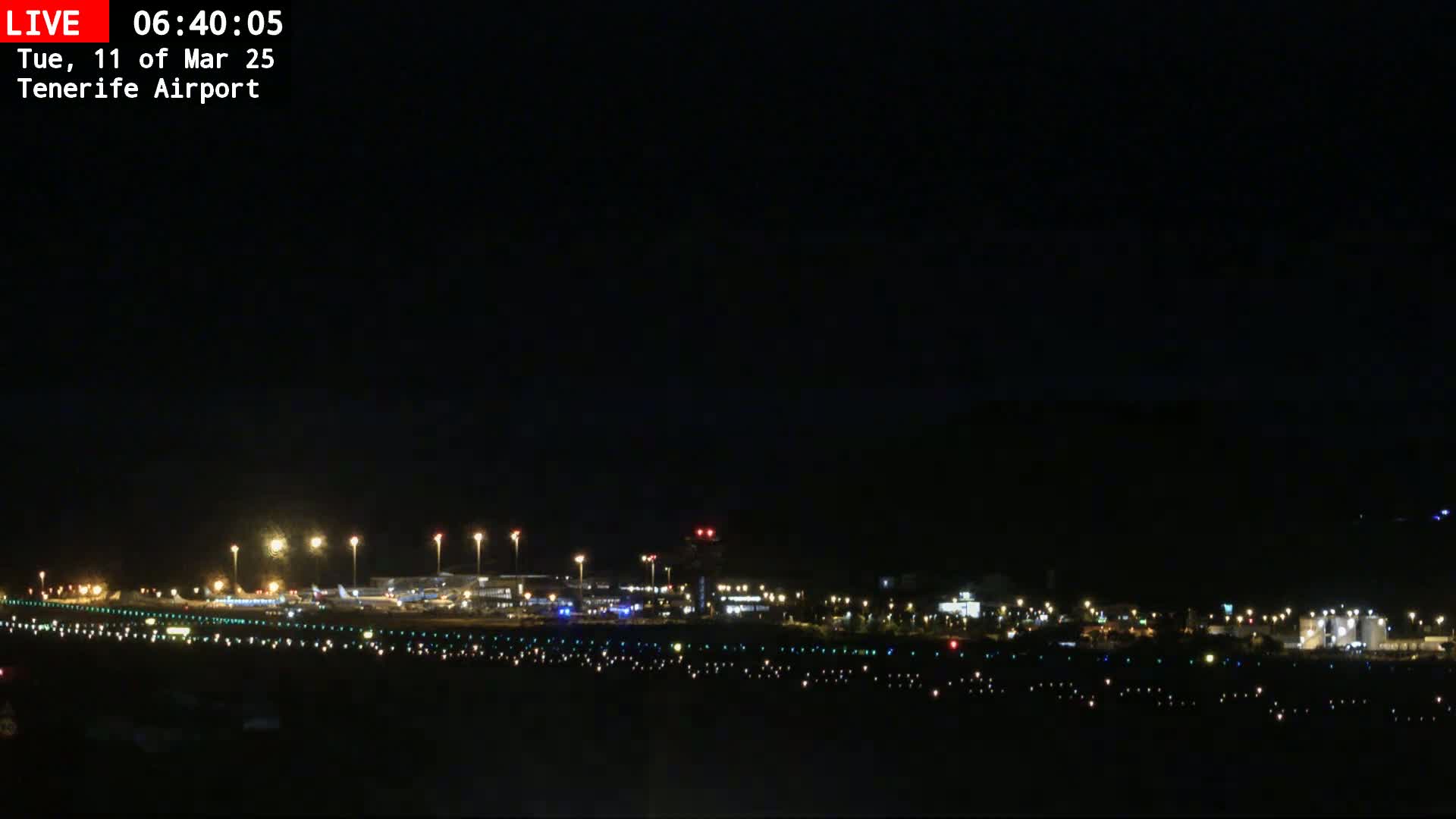 A nighttime, dark view of an airport runway with several lights illuminating the tarmac and buildings in the distance.
