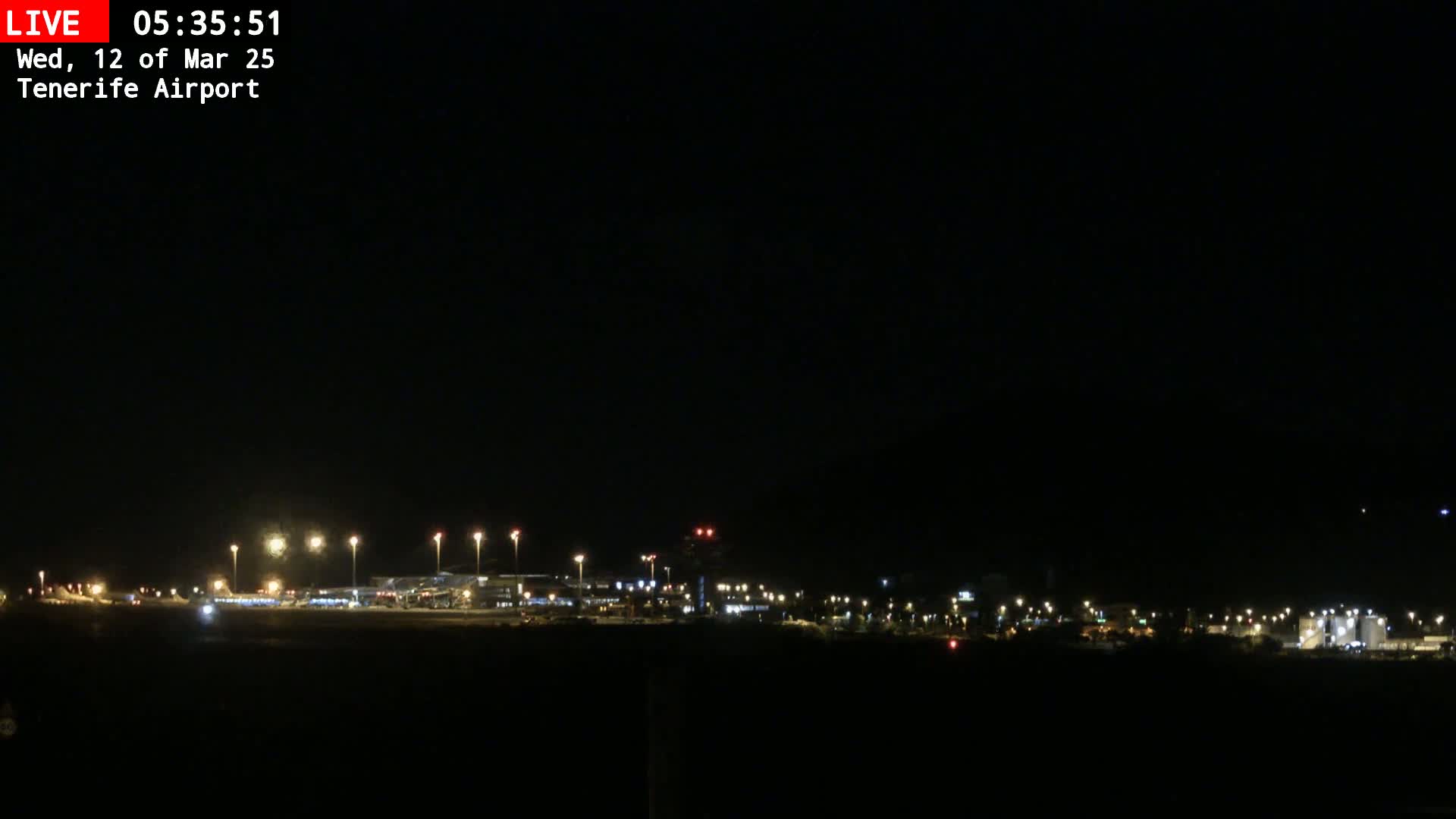 A nighttime view of an airport runway and terminal buildings illuminated by lights under a clear, dark sky.