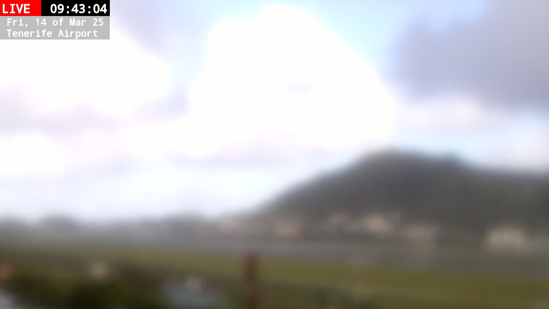 A blurry view of a hazy landscape with a hill in the background under a mostly cloudy sky.