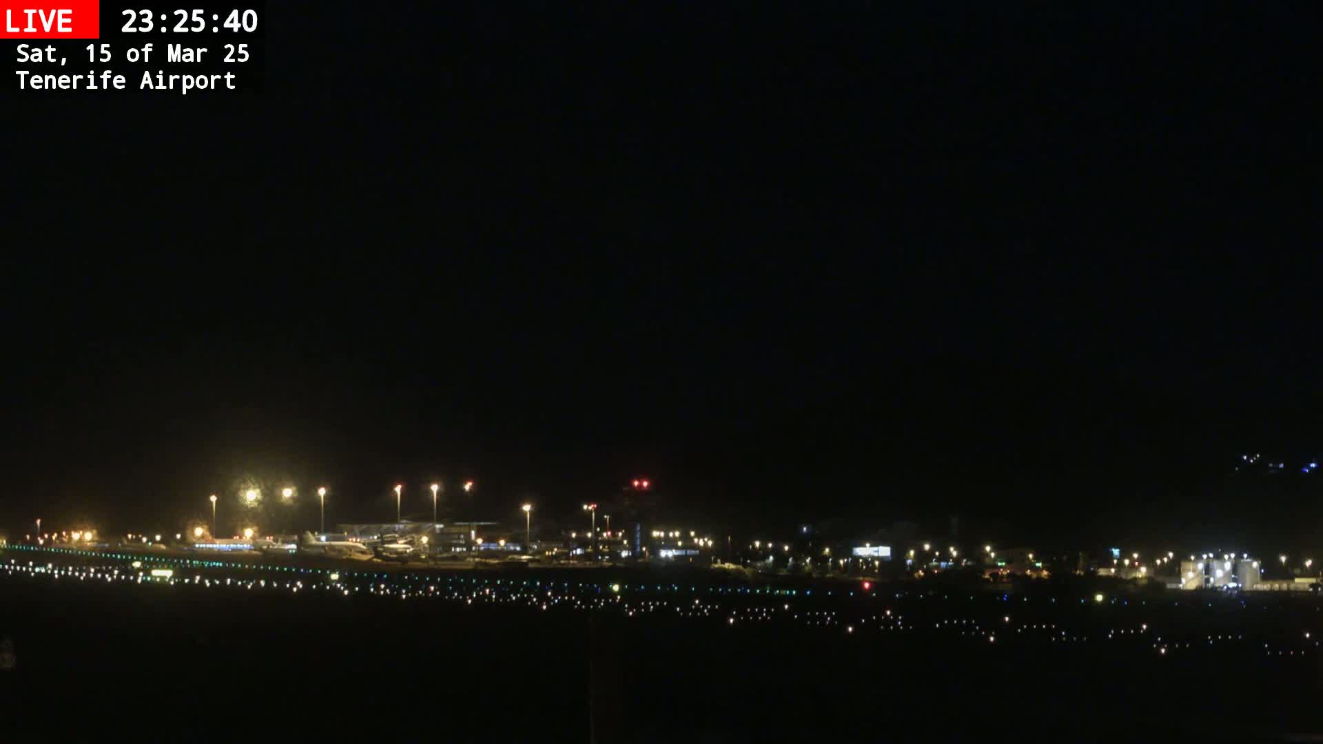 A nighttime view of an airport runway and terminal buildings illuminated by lights under a clear, dark sky.