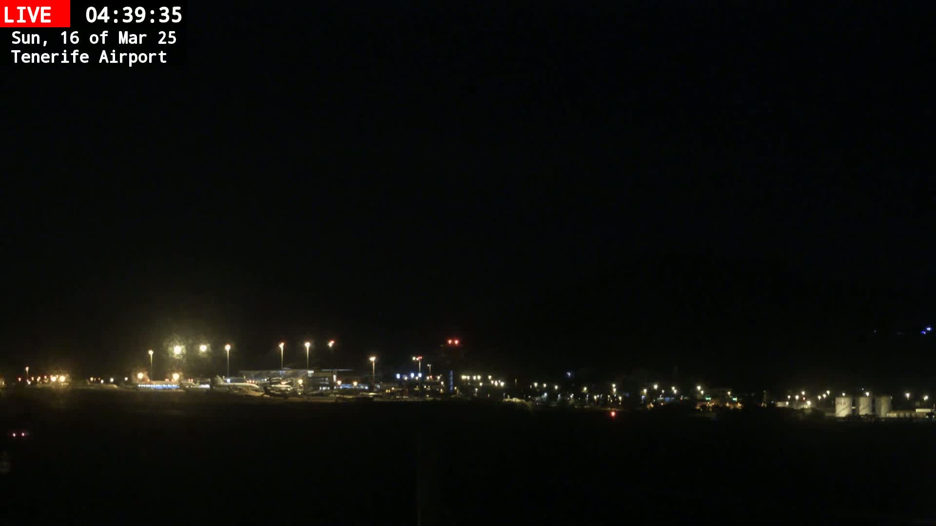A nighttime view of an airport runway and terminal buildings illuminated by artificial lights under a dark, clear sky.
