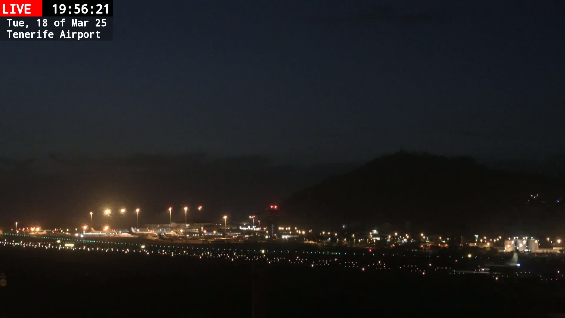 A nighttime view of an airport runway and surrounding buildings illuminated under a dark, clear sky.